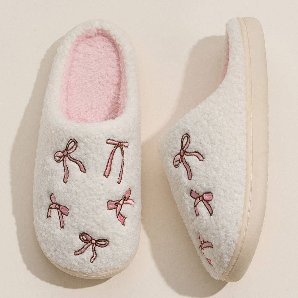 Pair of light gray slippers with pink bows on a beige background