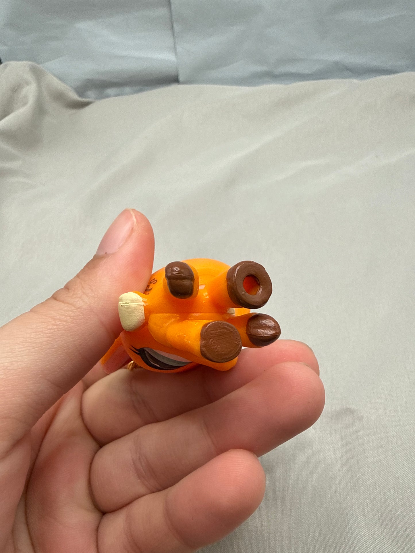 Hand holding a small orange and brown figurine against a plain background