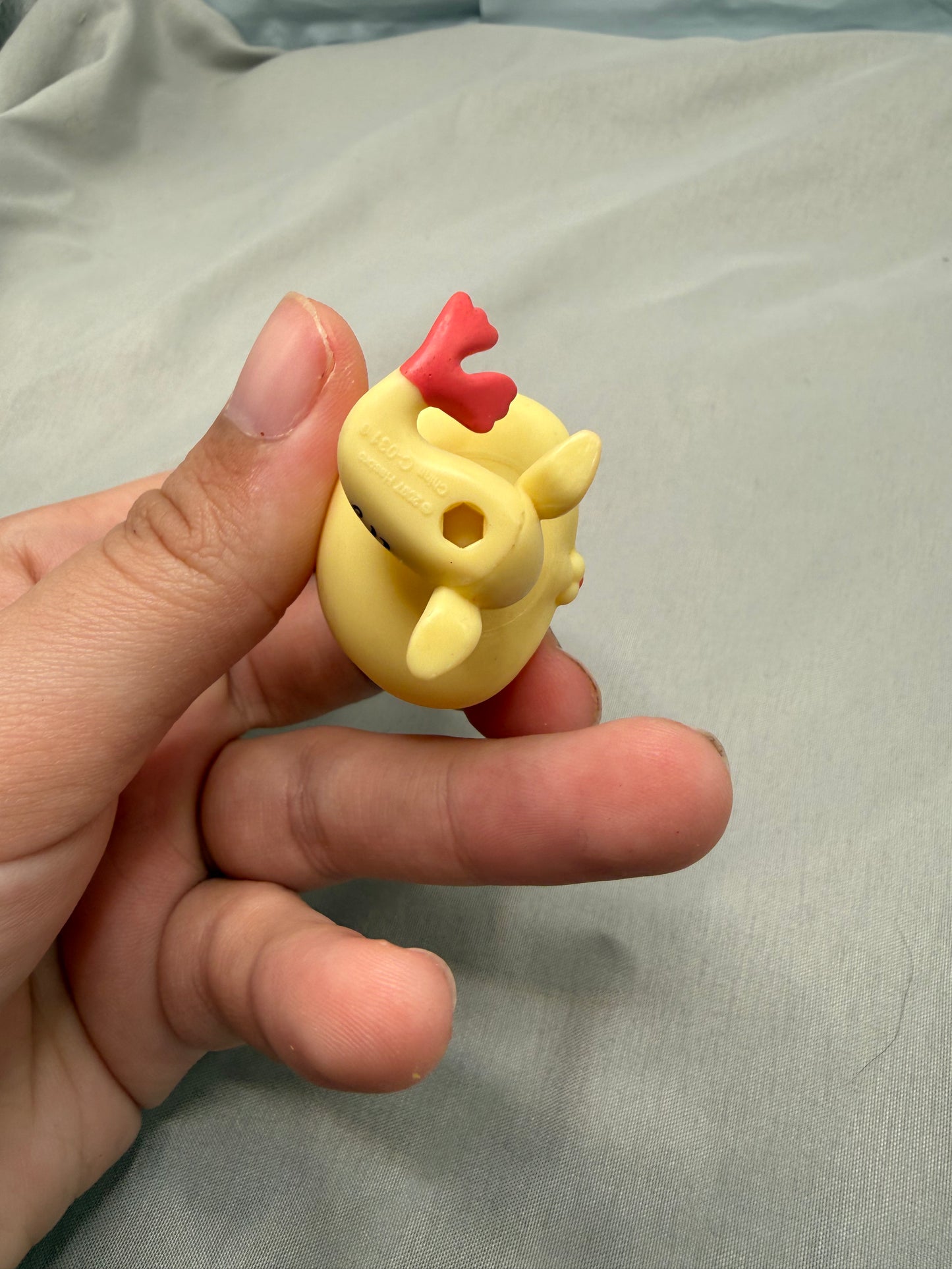 Hand holding a small yellow rubbery seal with red fin against a light gray background