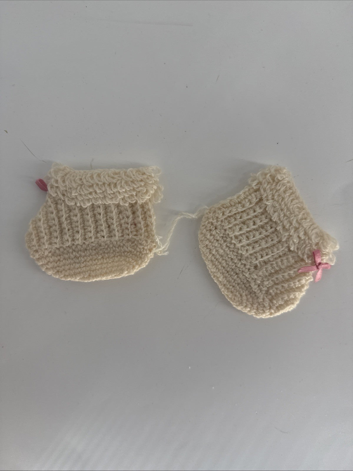 Pair of beige crocheted baby booties on a light gray background