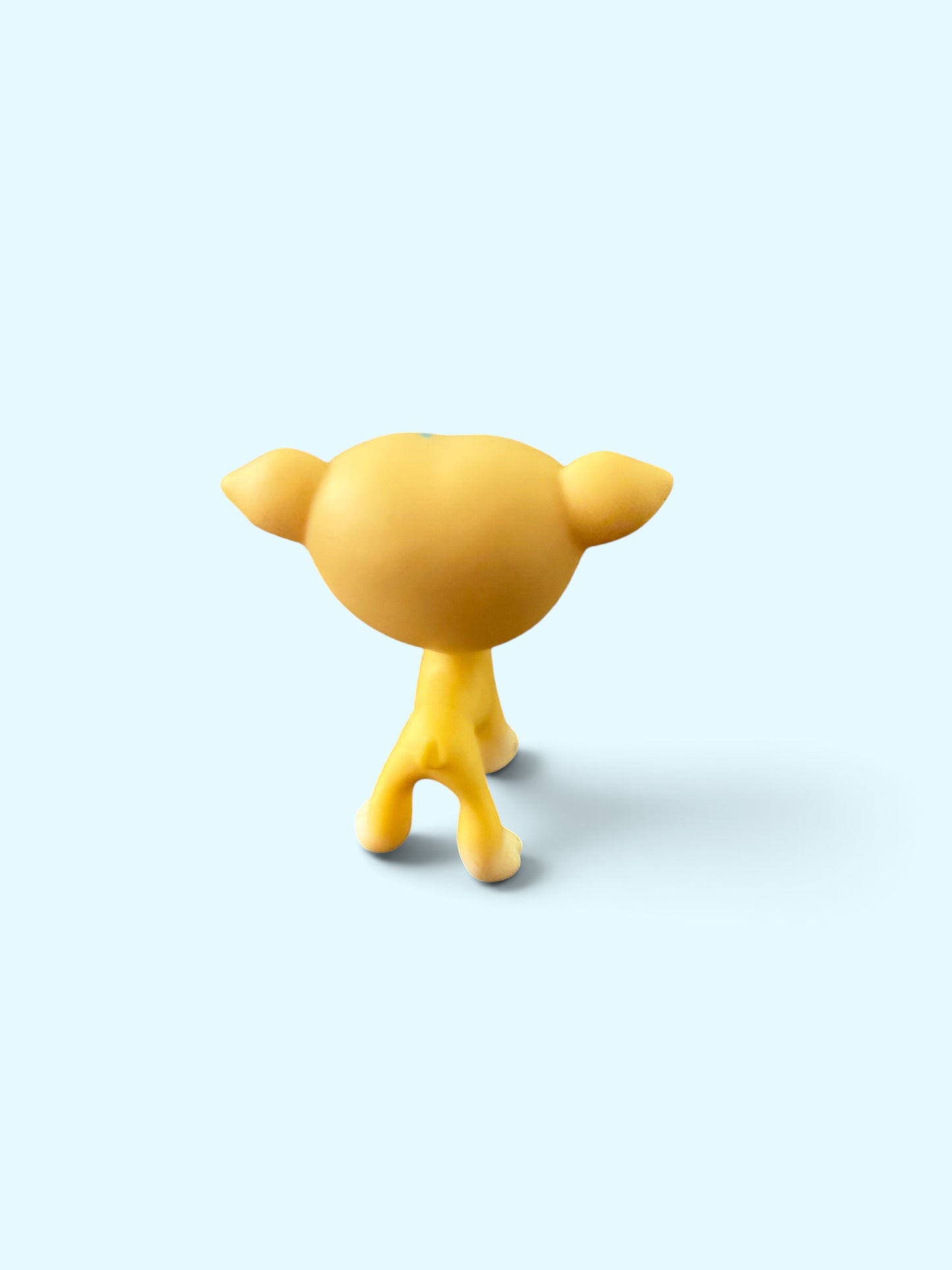 A small yellow cartoon figurine with a round head, two small ears, and four legs, shown from the back on a light blue background.