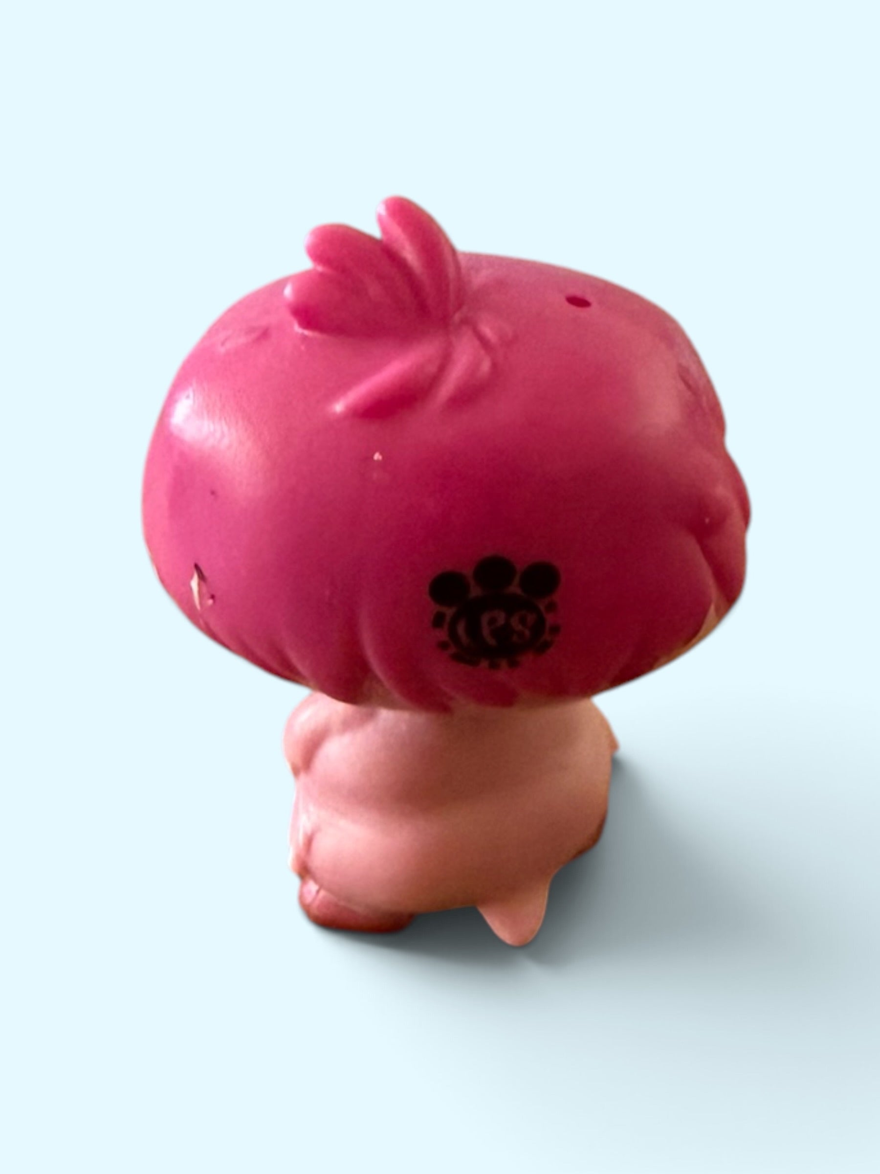 A small pink mushroom-shaped toy or figurine with a darker pink cap and a pale pink stem, photographed on a light blue background.