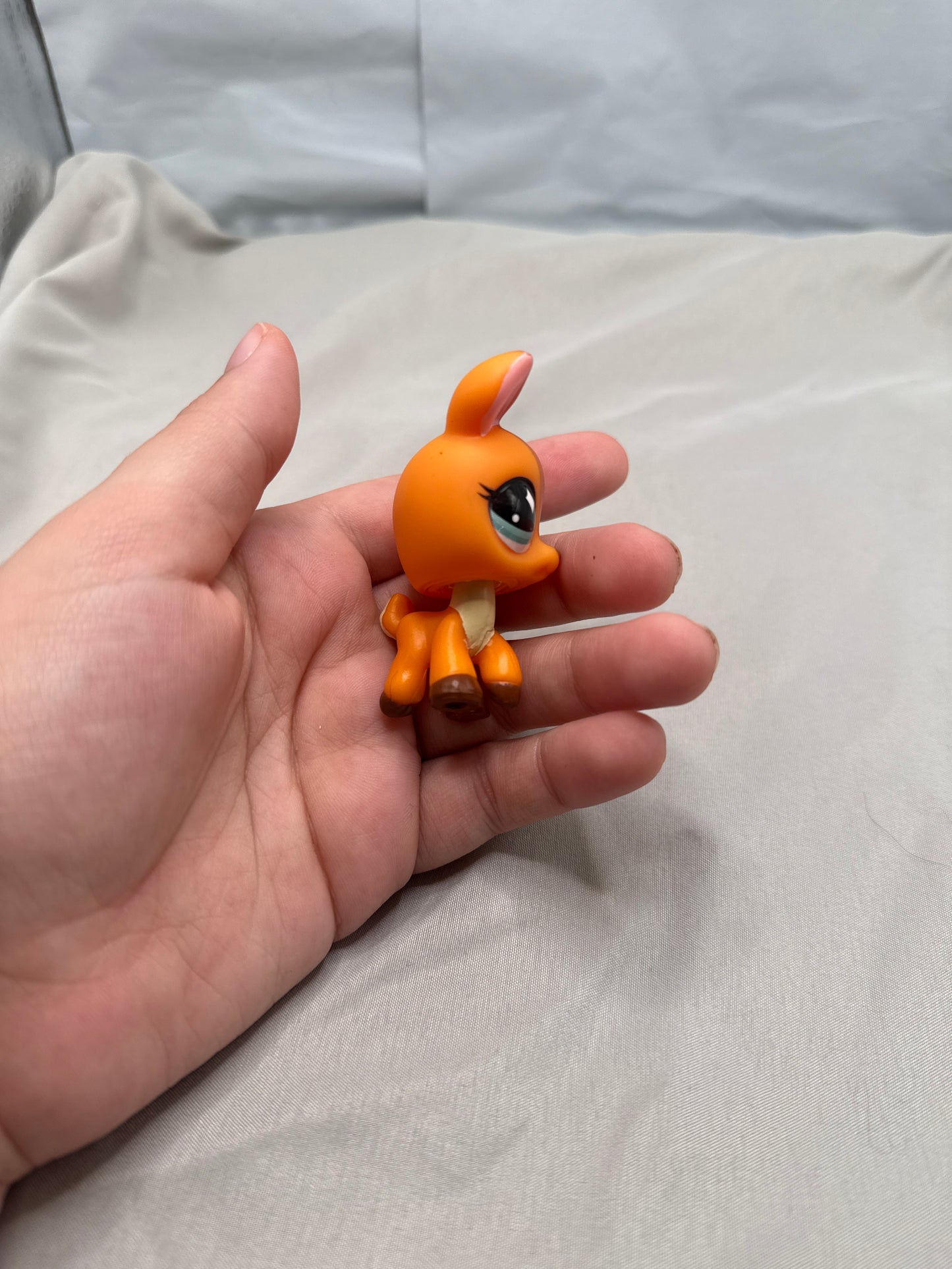 Hand holding a small orange figurine against a neutral background