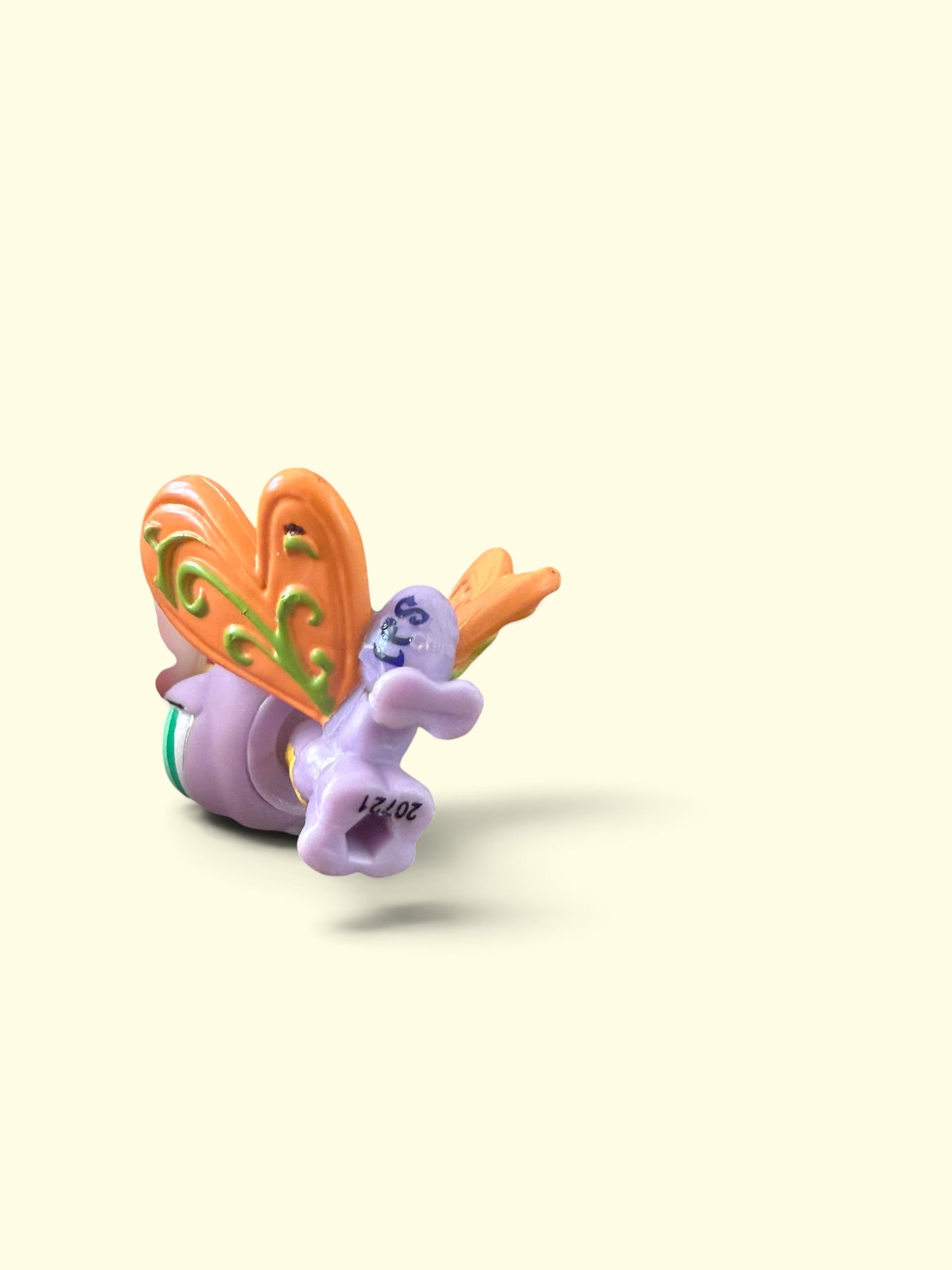 A small decorative figurine of a purple creature with orange and green patterned wings, shown on a plain cream background.