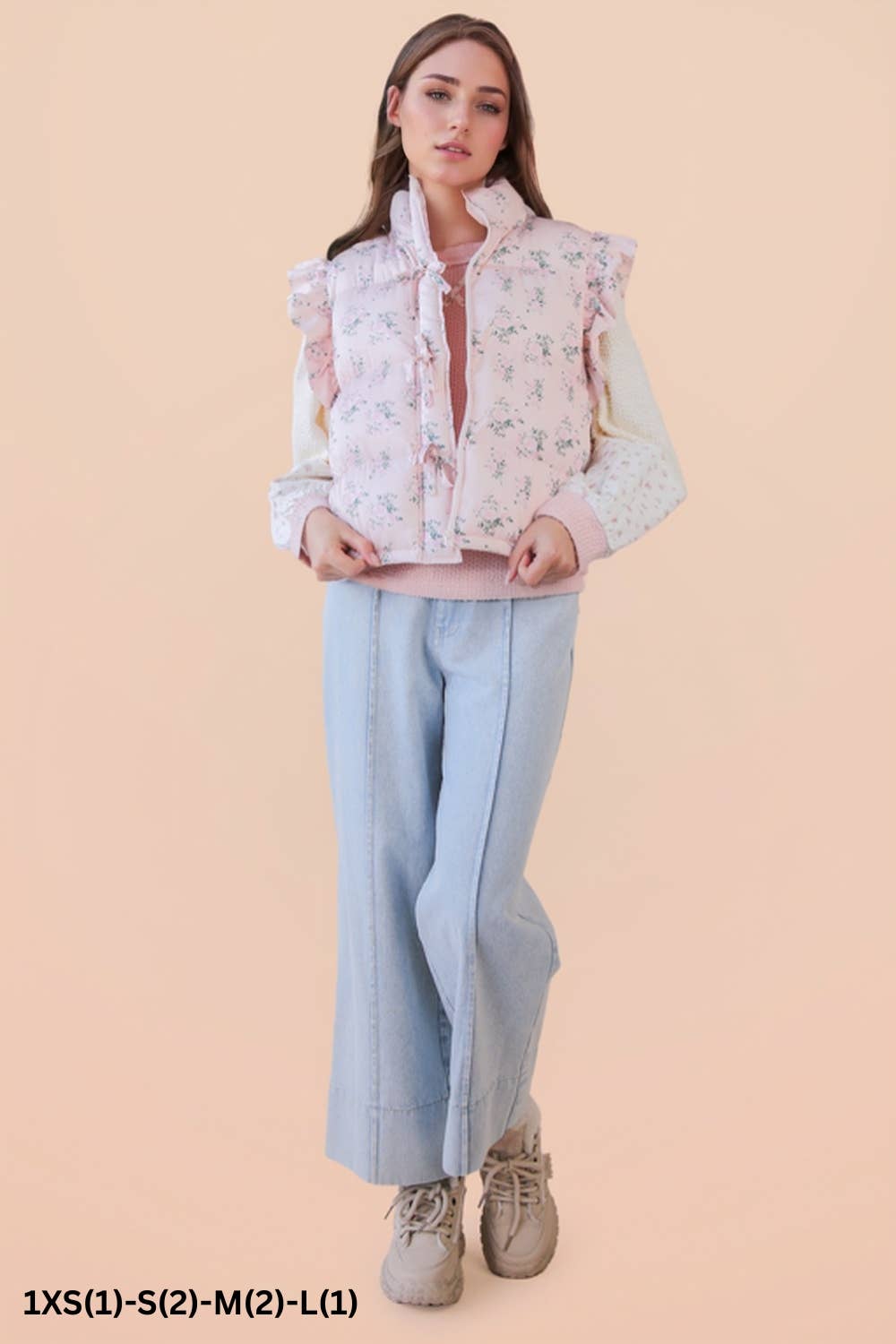 Woman wearing a floral puffer vest  and light blue pants on a beige background