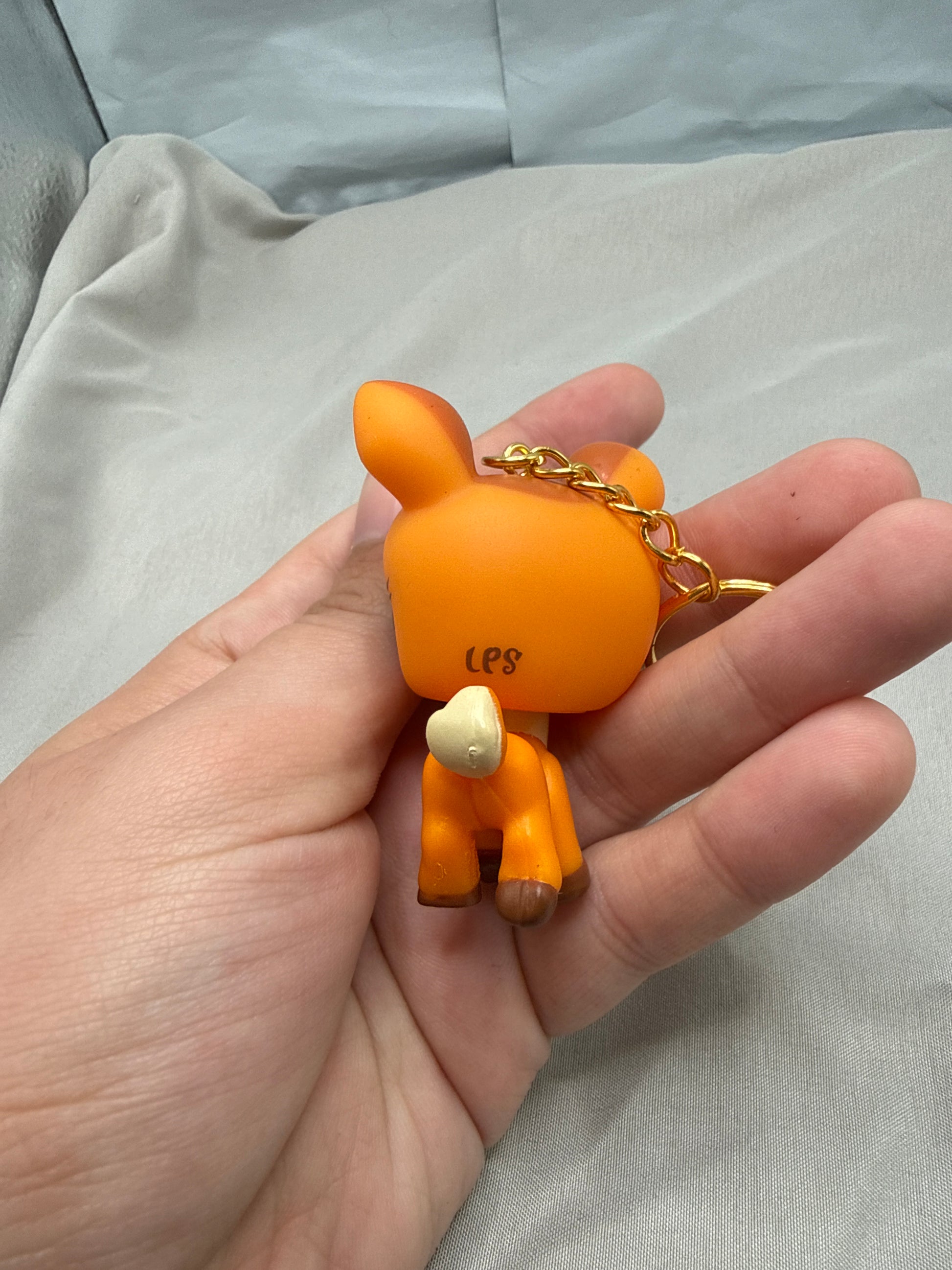 Hand holding an orange keychain with a small gold chain against a light gray background