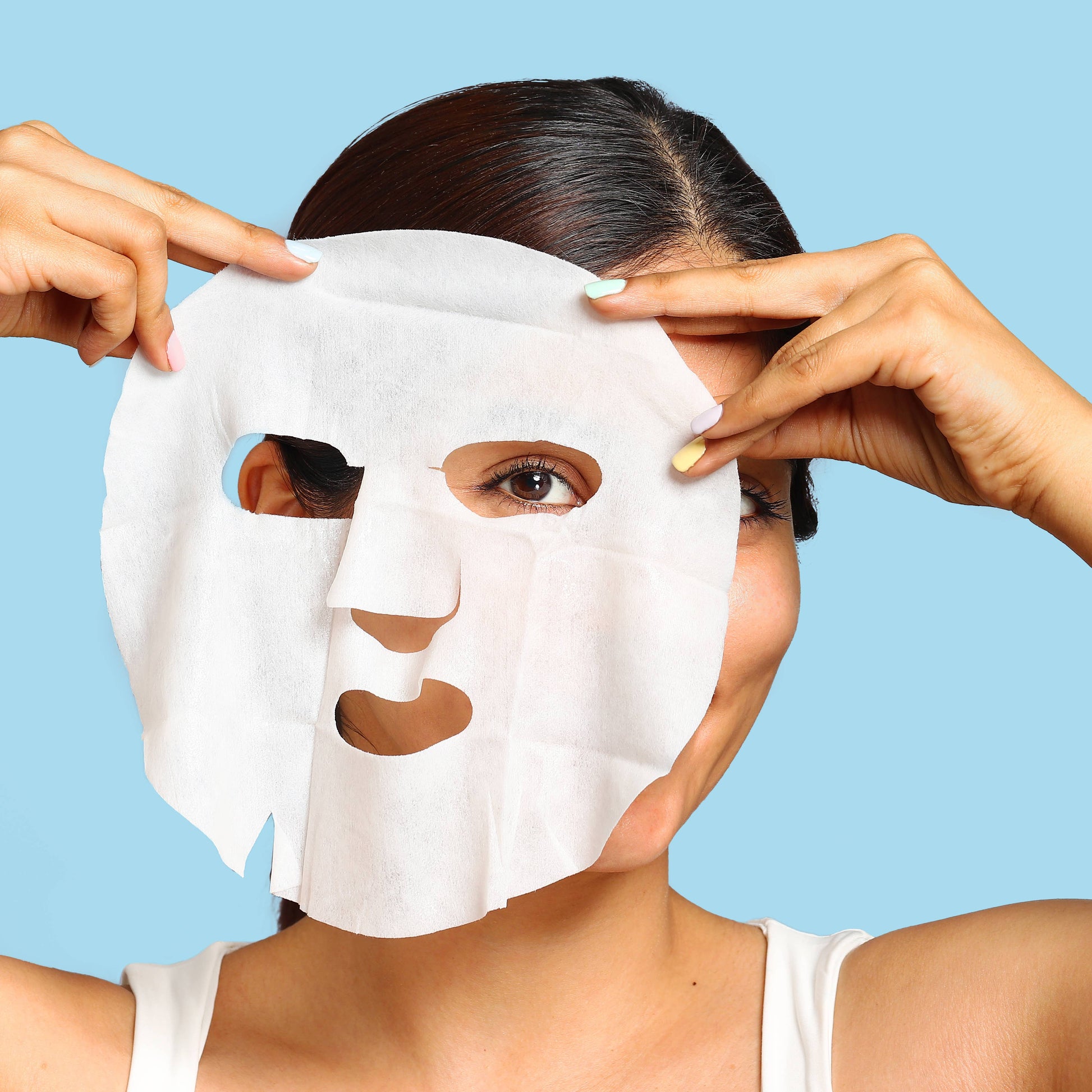 Person applying a white face mask against a blue background
