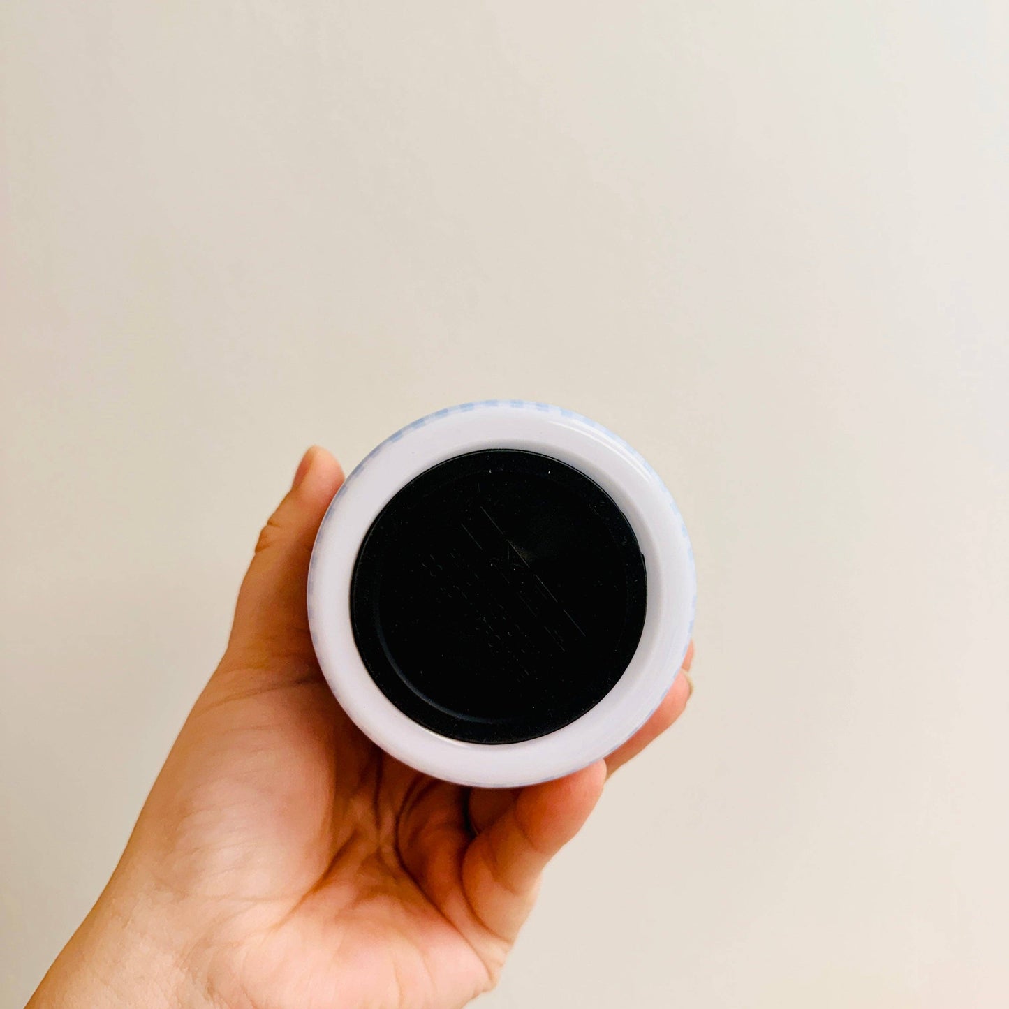 Hand holding a small round object with a black center against a plain background