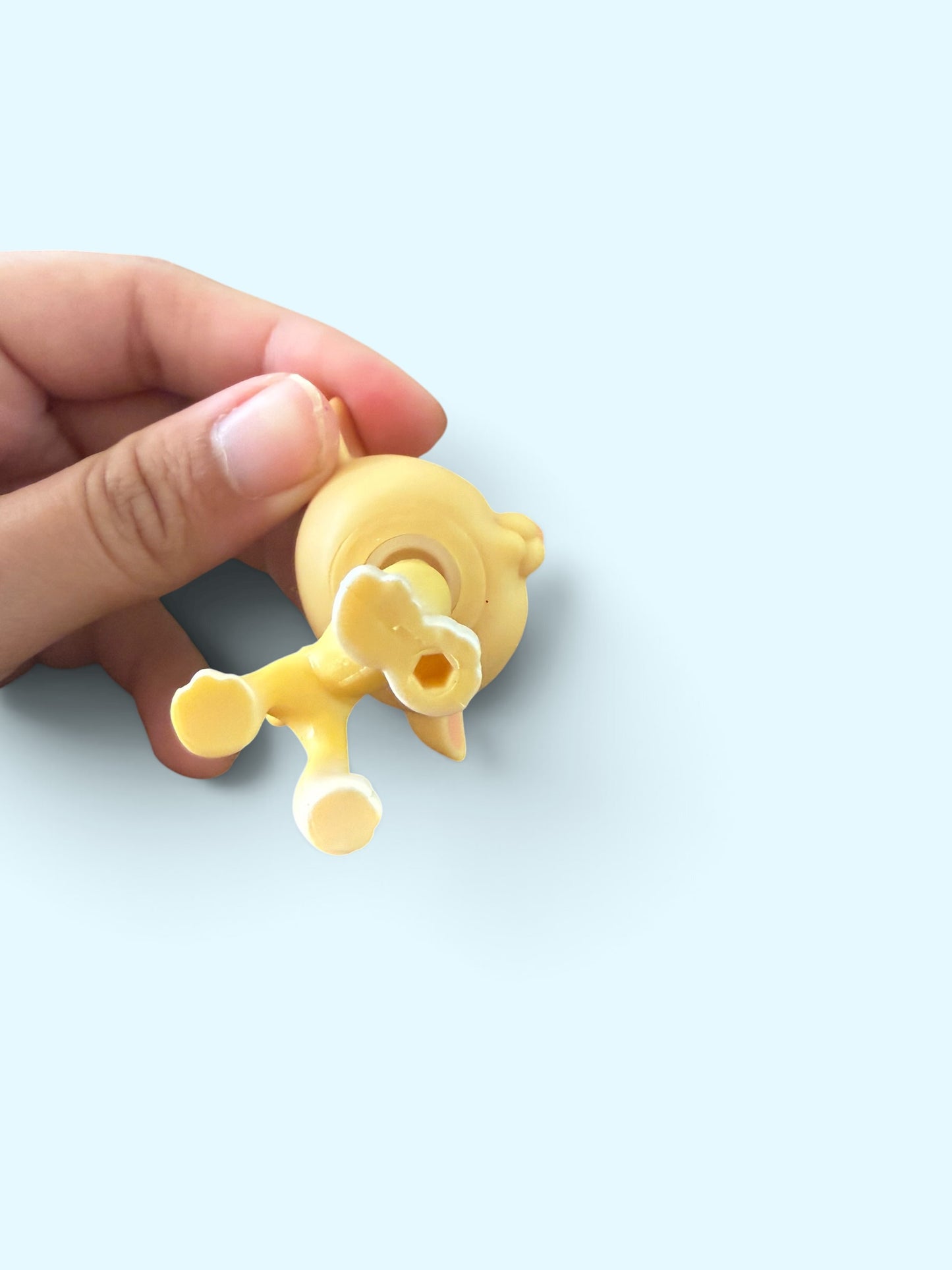 A hand holding a small yellow plastic accessory against a solid light blue background.