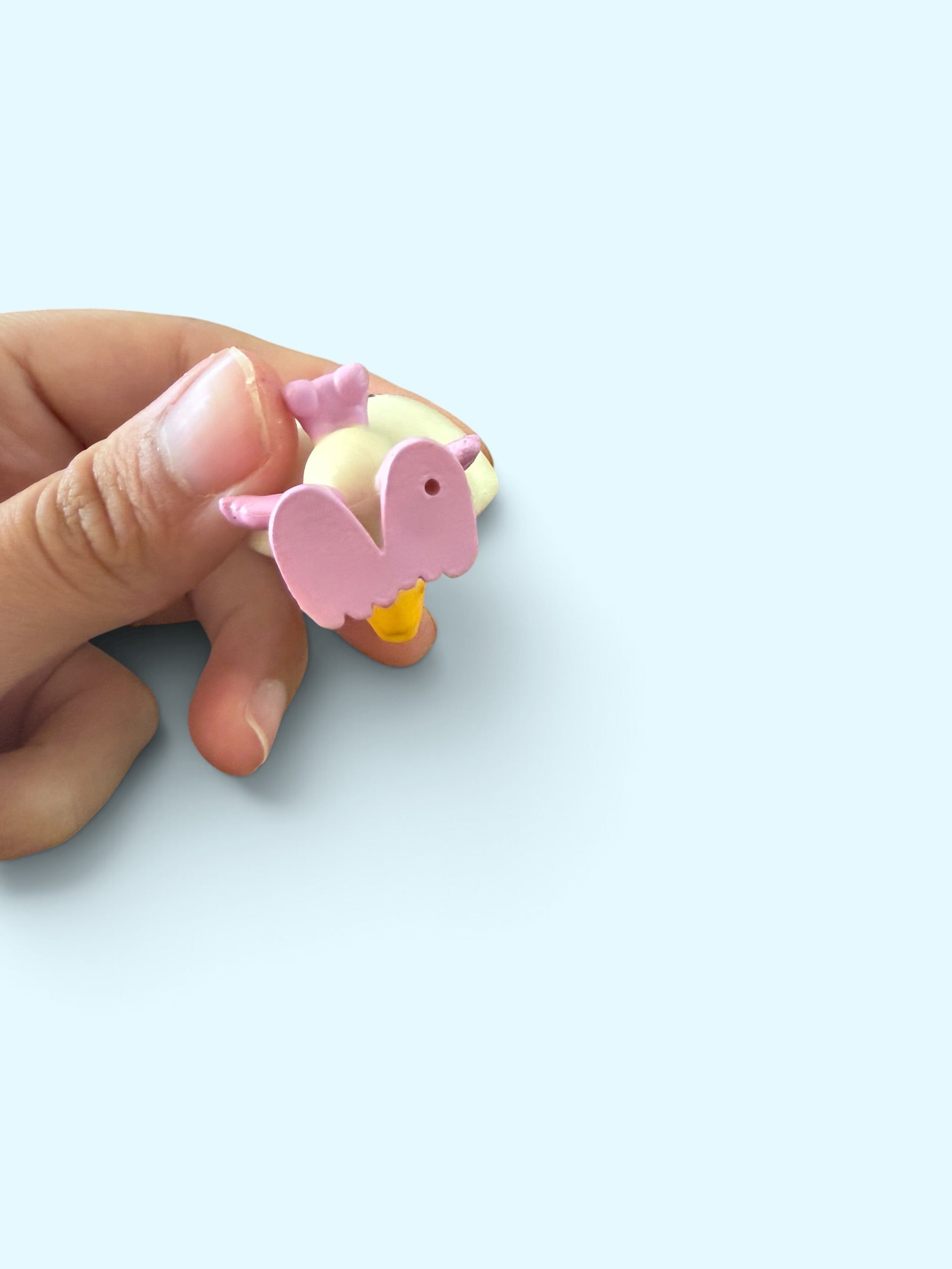 A hand holding a small pink and yellow bird-shaped accessory against a light blue background.