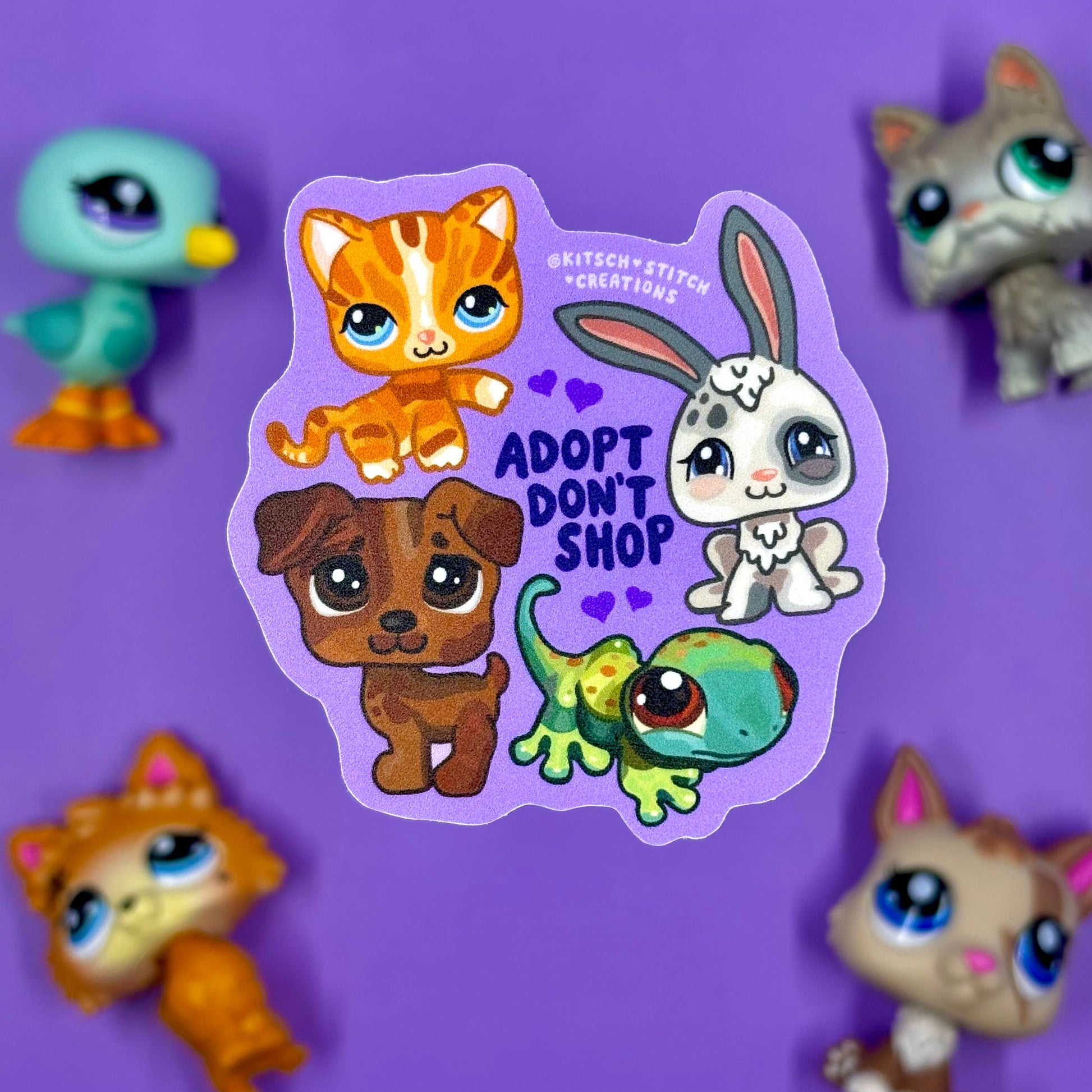 Sticker with cartoon animals and 'Adopt Don't Shop' text on a purple background with toy figurines.