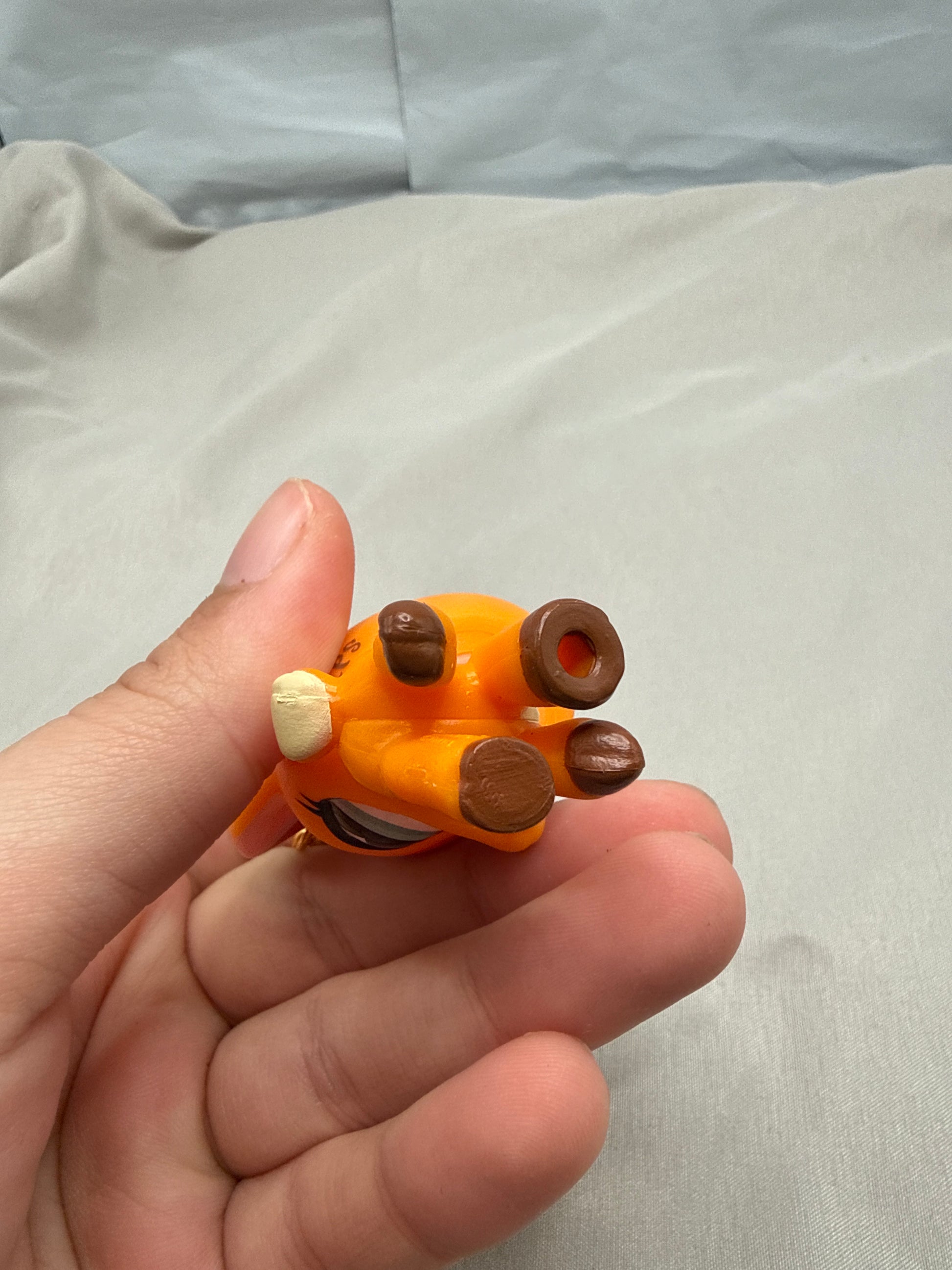 Hand holding a small orange and brown figurine against a plain background