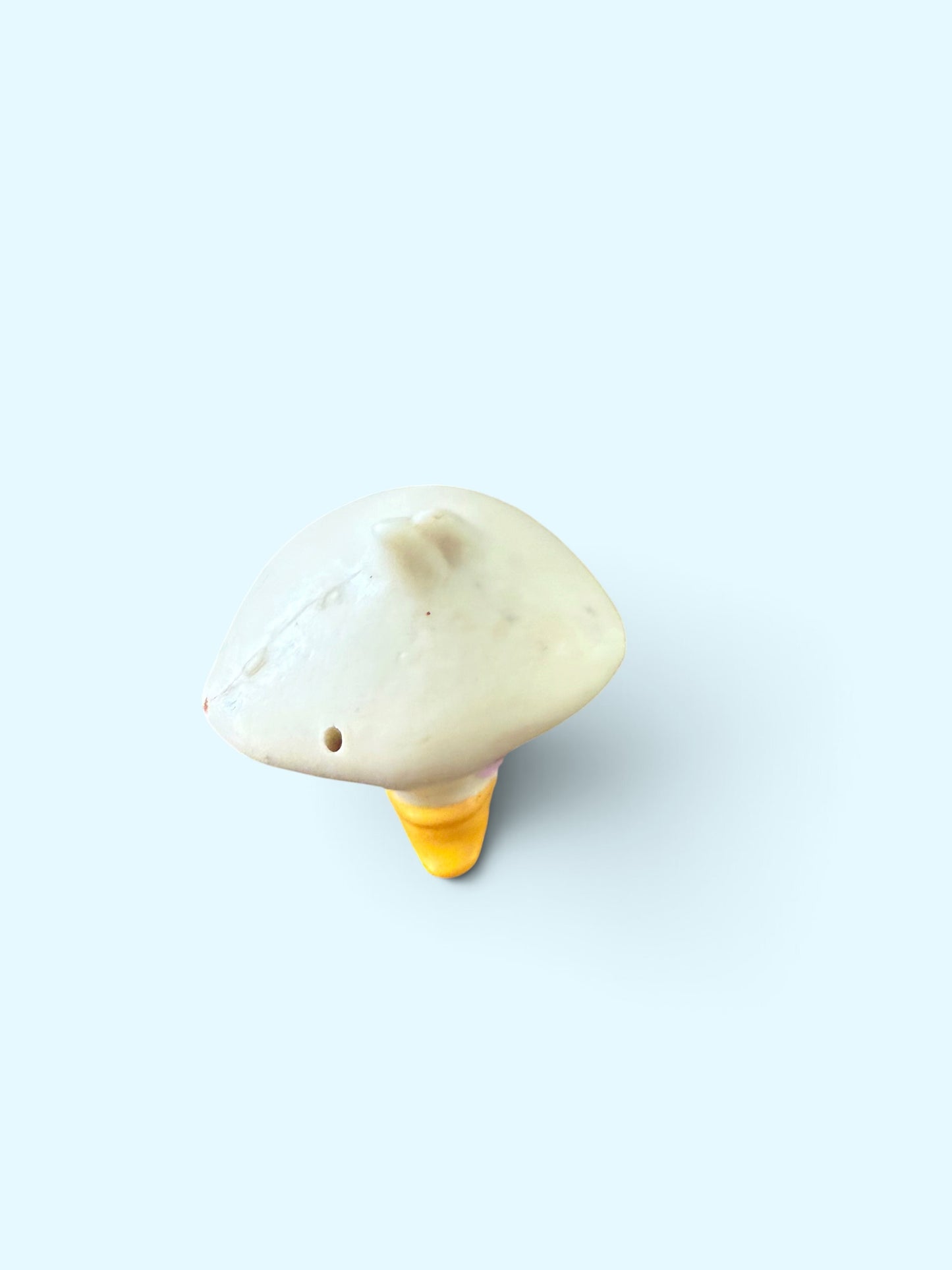 A small head-shaped decorative object with an off-white cap and a yellow stem, photographed on a plain light blue background.