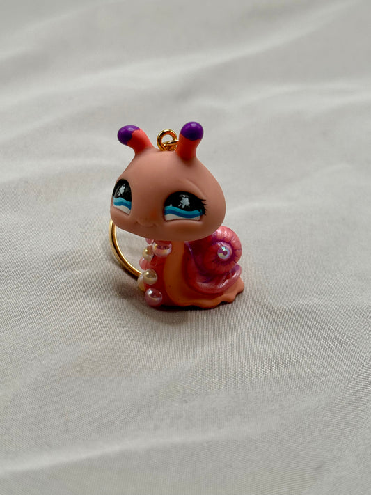 Small figurine of a pink creature with purple eyes on a white fabric background