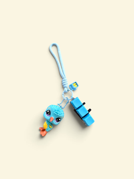 A light blue silicone carabiner clip with a cute blue bird charm and a blue rectangular accessory, displayed on a solid cream-colored background.