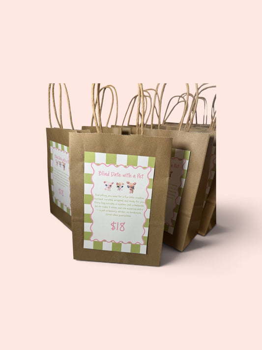 Three brown kraft paper gift bags with twisted paper handles, each featuring a decorative front label with green and white stripes and pink text, set against a solid pale pink background.