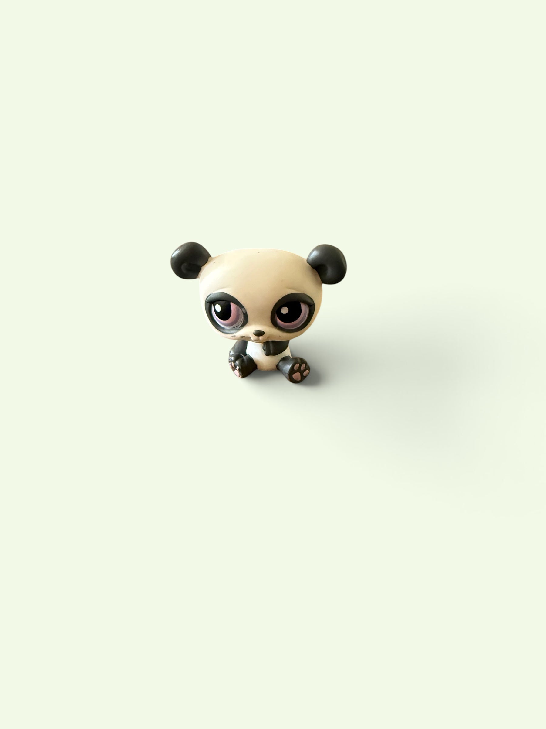 A small stylized panda figurine with large glossy eyes, sitting centered on a plain off-white background.