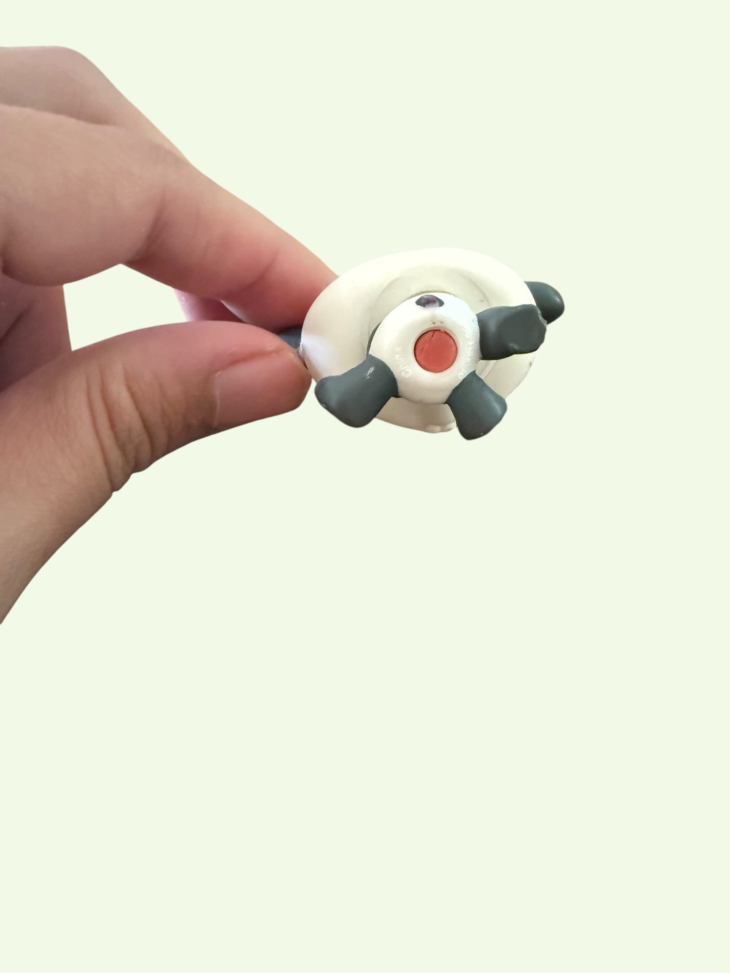 A hand holding a small white and gray toy figure with a red circular detail, shown against a plain light background.