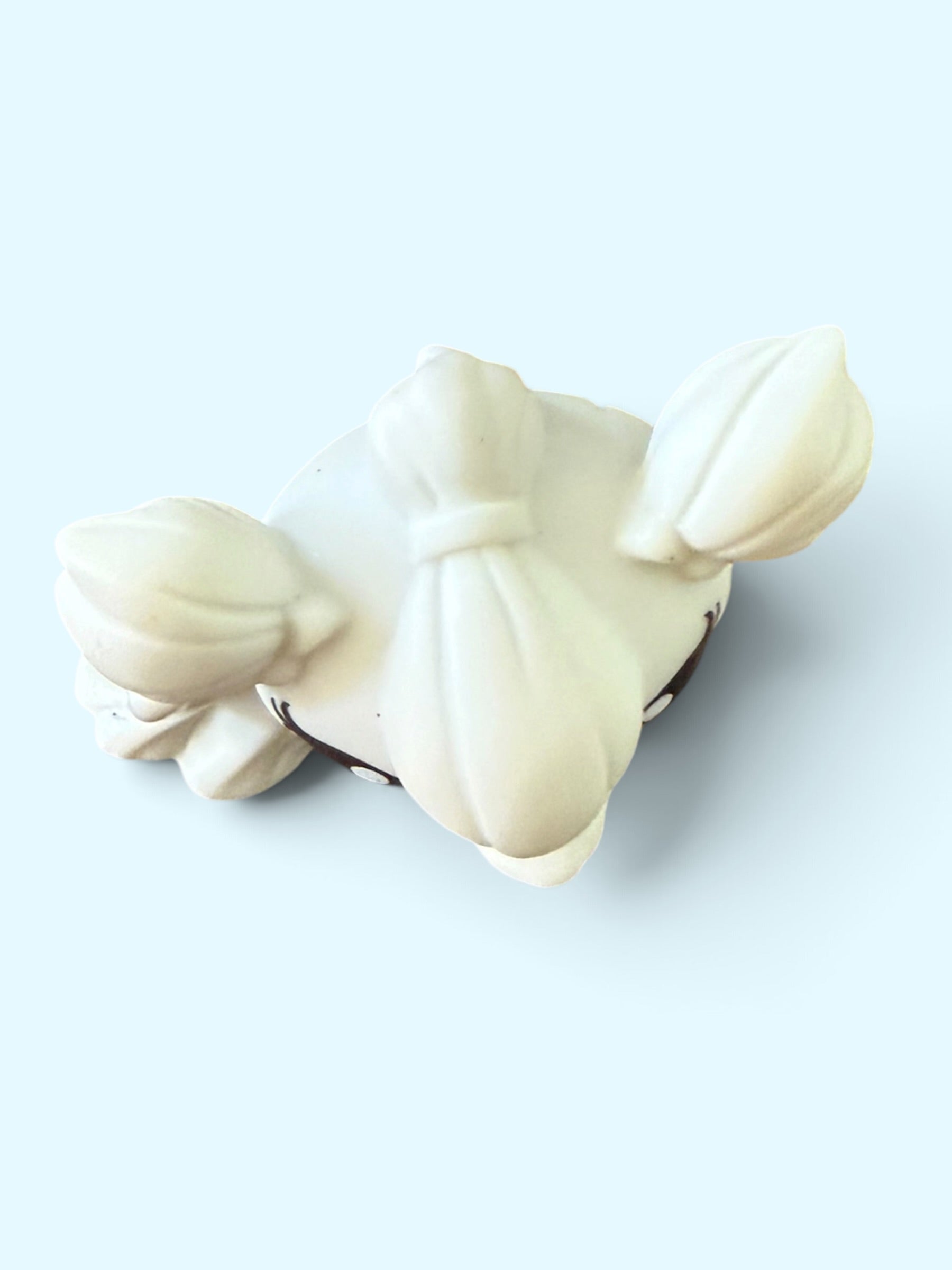 An off-white ceramic figurine shaped like a stylized bow and arrow, photographed on a light blue background.