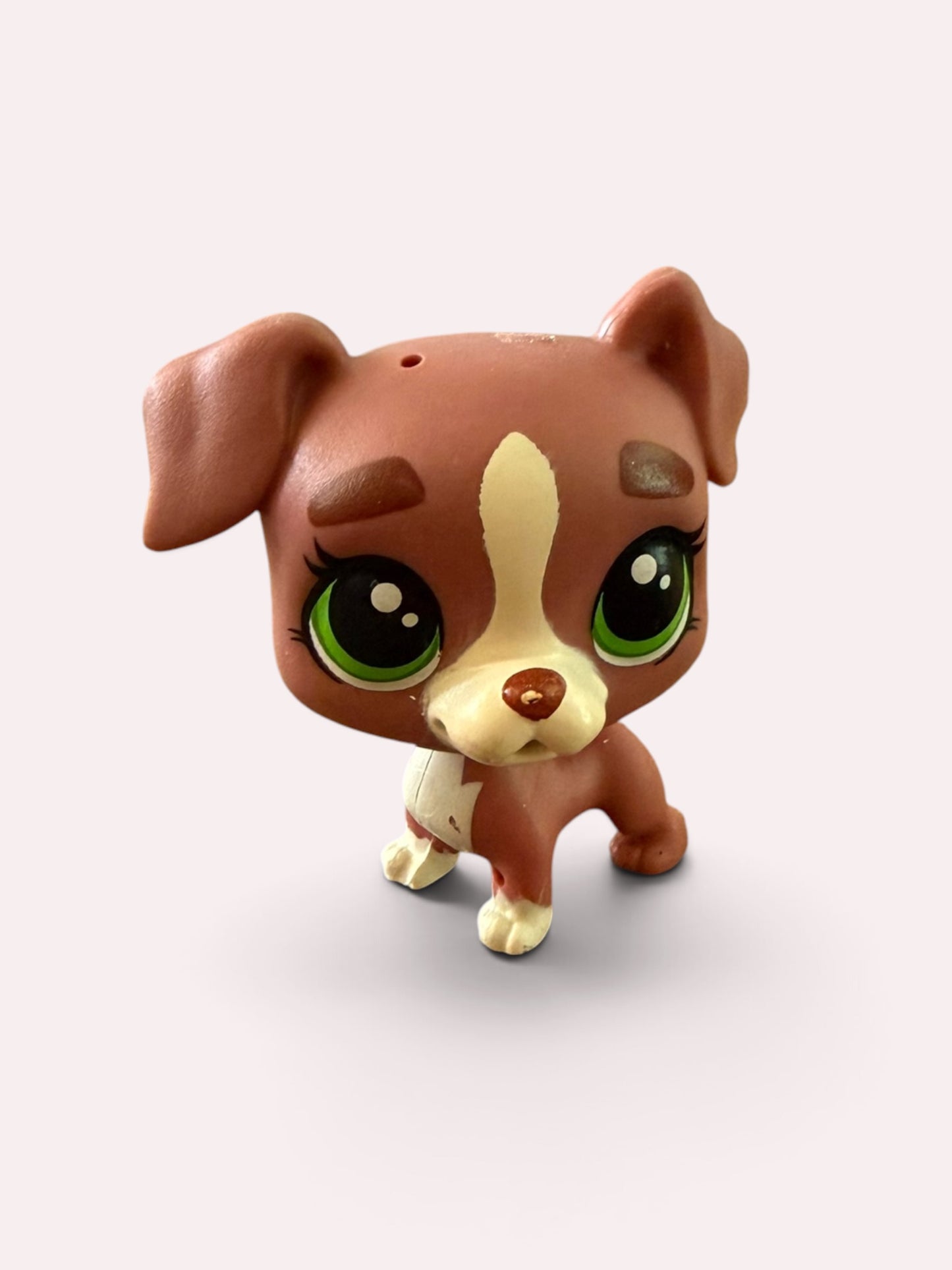 A small brown toy dog figurine with large green eyes, a cream-colored snout and paws, and floppy ears, photographed against a plain light background.