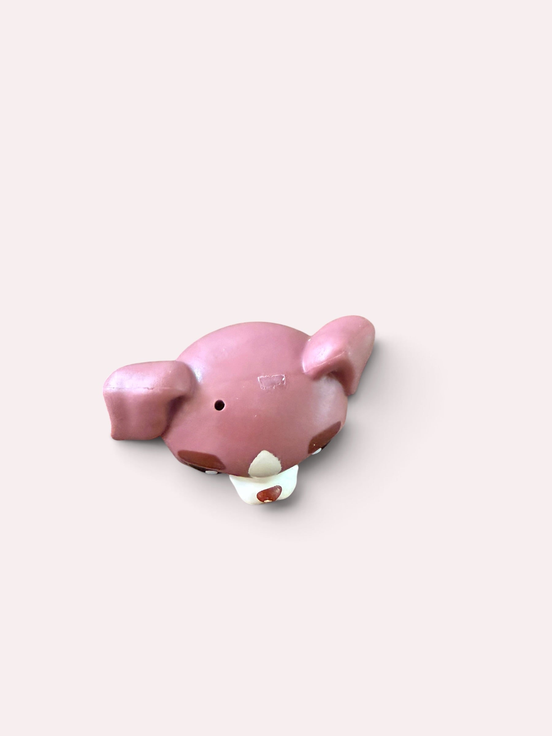 A pink dog-shaped product, possibly a piggy bank or decorative figurine, featuring floppy ears, a small black eye, and a white bib with a small red heart, set against a solid pale pink background.