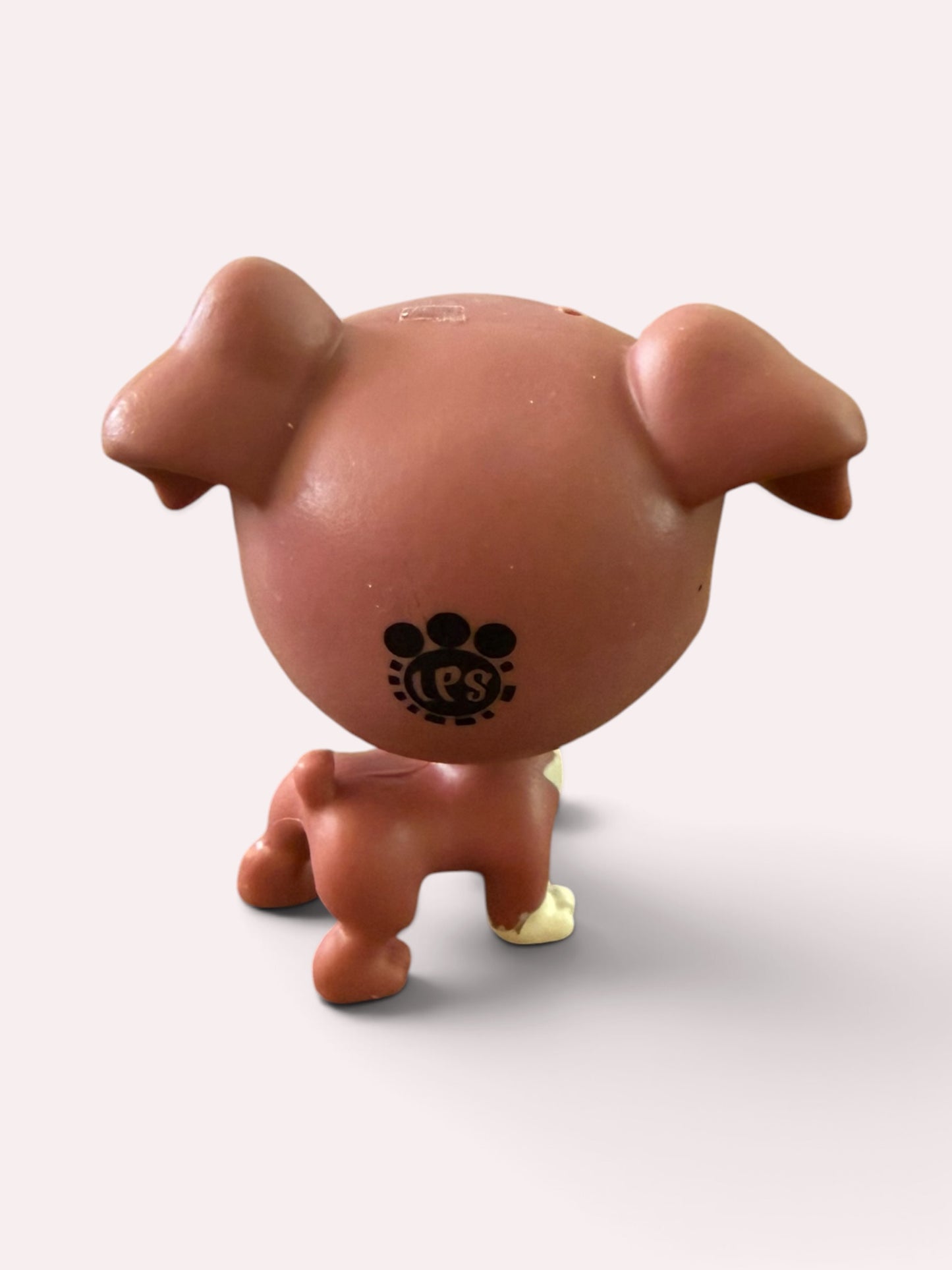 A small stylized dog figurine shown from the back, with a round head, floppy ears, and a black paw-print style logo on the back, photographed against a plain light background.