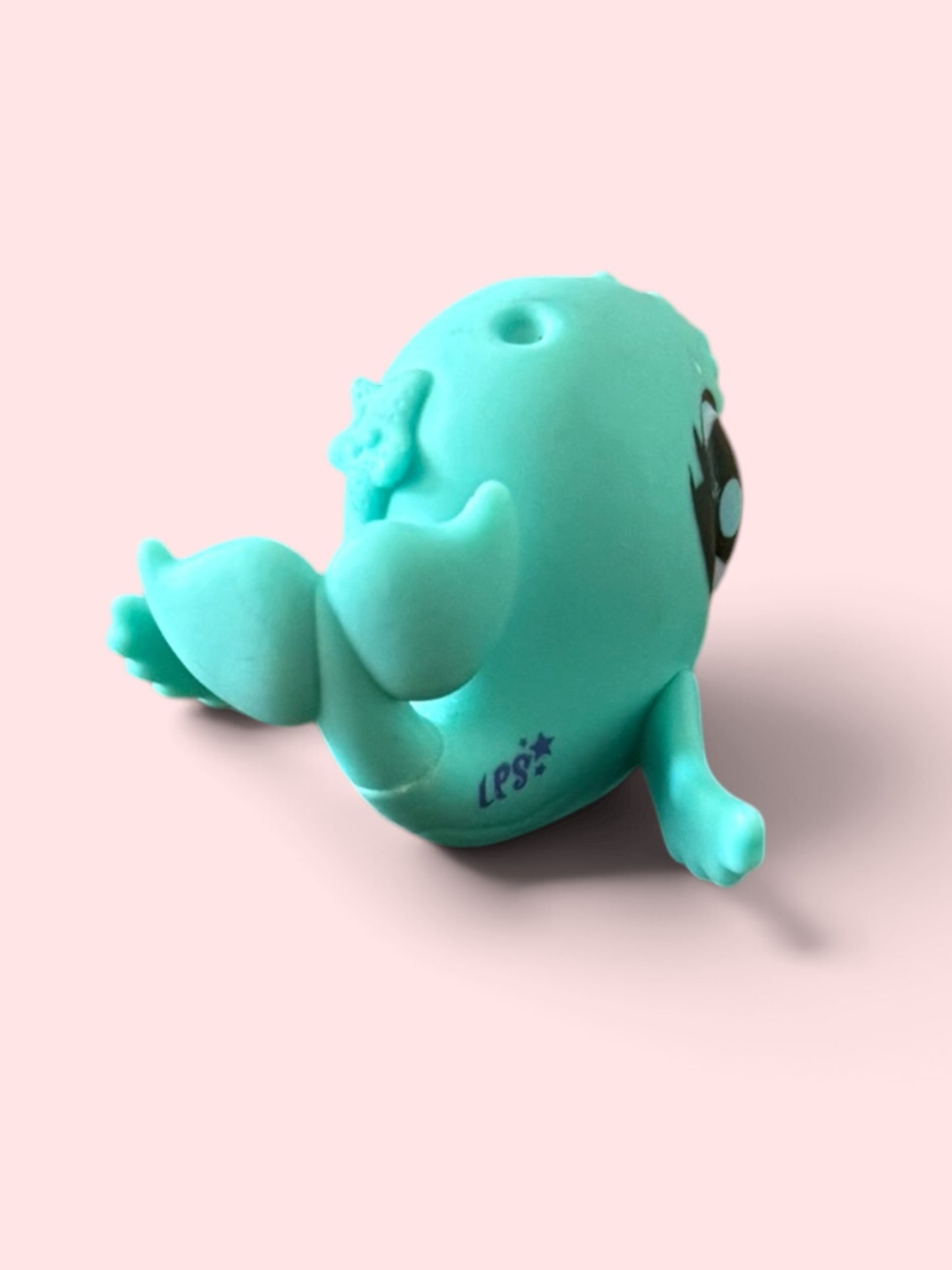 A mint green silicone novelty toy shaped like a stylized whale or sea creature, shown on a solid pale pink background.