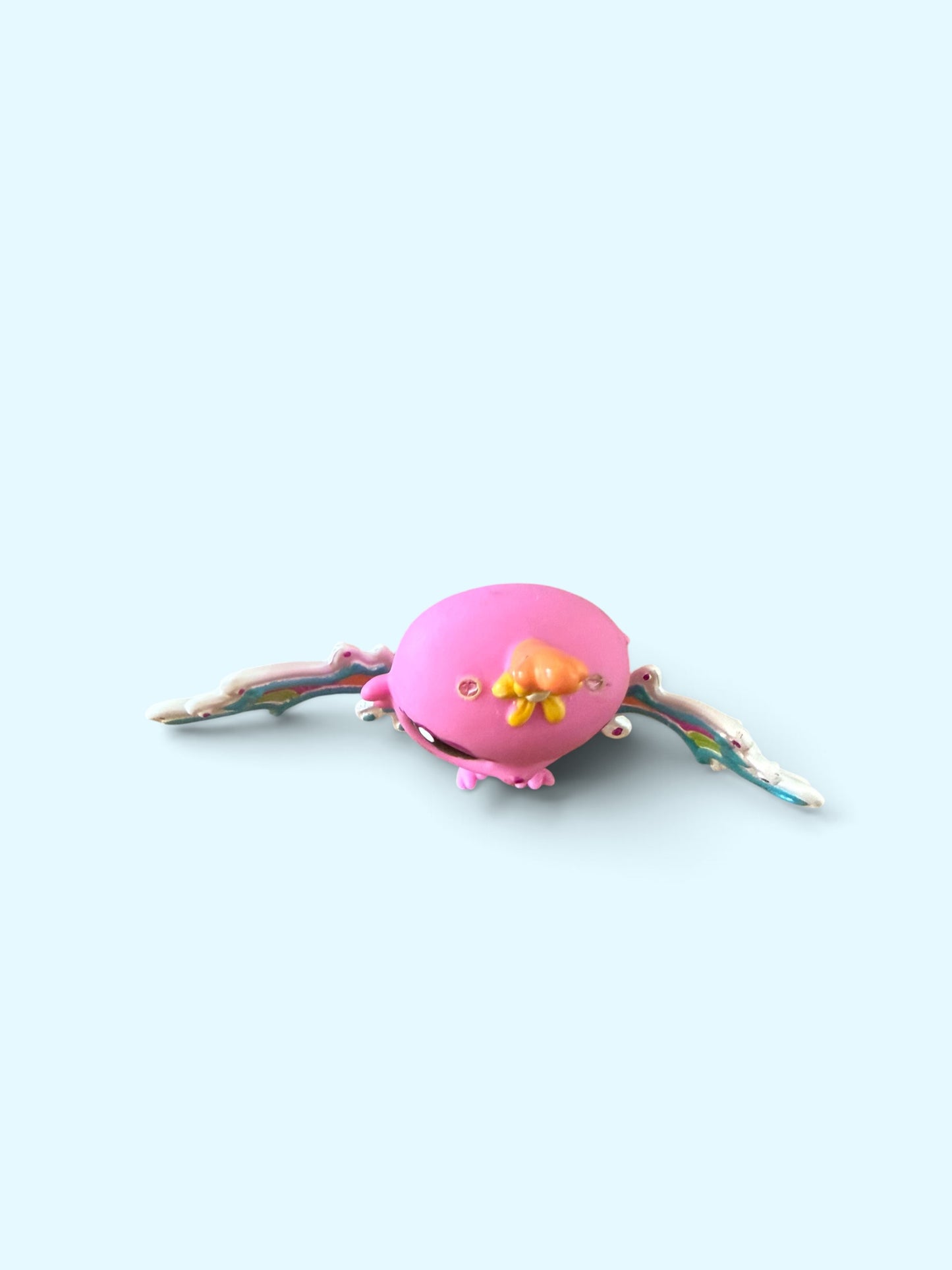A small pink bird figurine with colorful wings and yellow beak details, centered on a light blue background.
