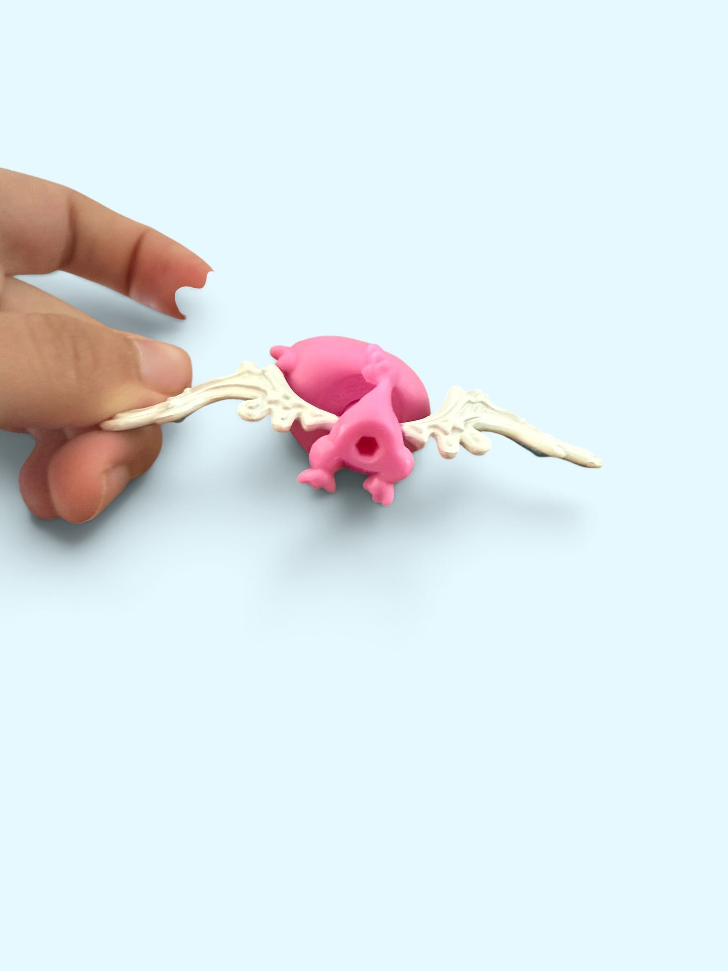 A small pink winged toy or figurine being held by a person's fingers against a light blue background.