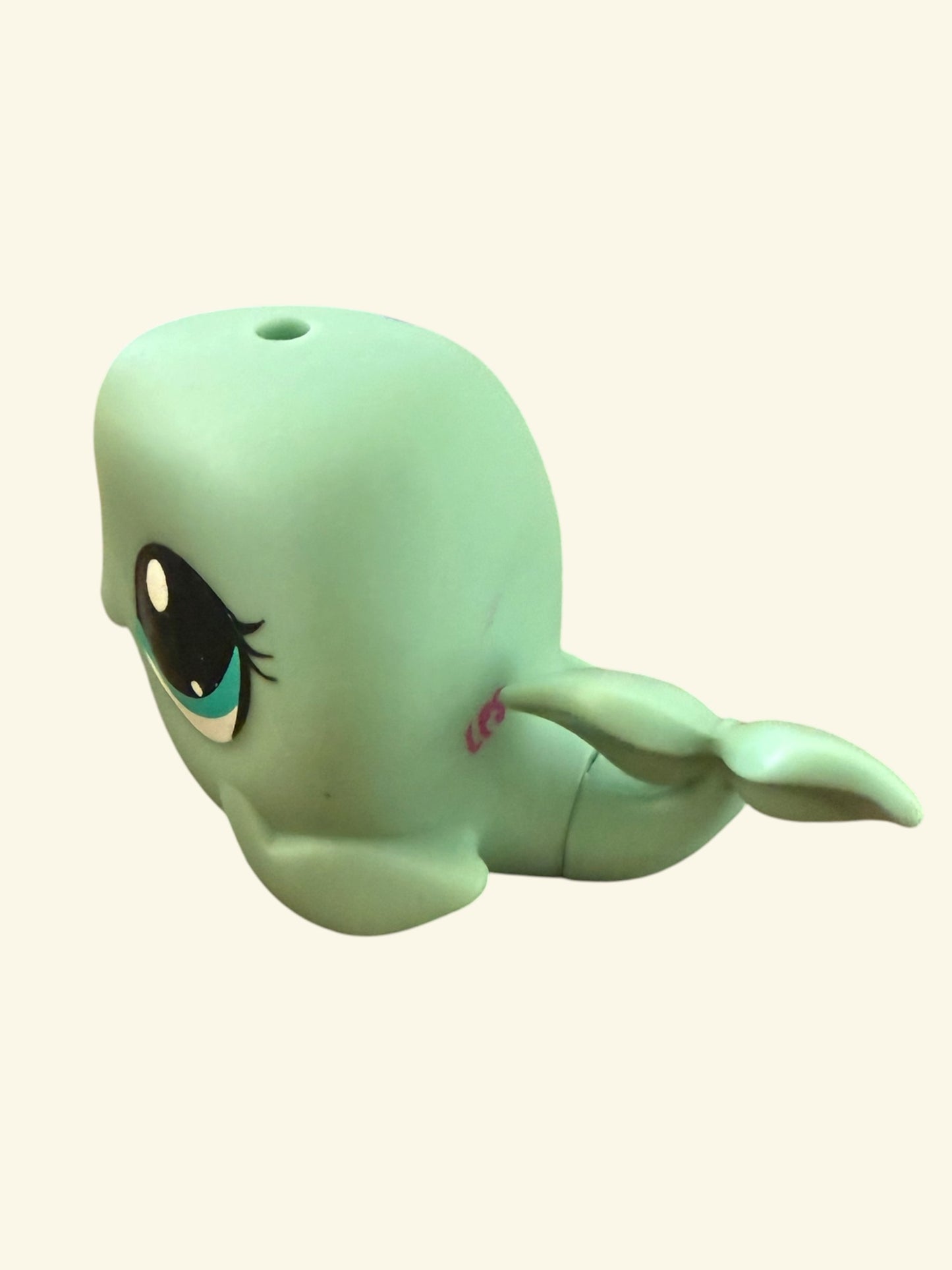 A mint green whale-shaped plastic toy or container with a large cartoon eye and a small pink detail on its side, shown against a plain light beige background.