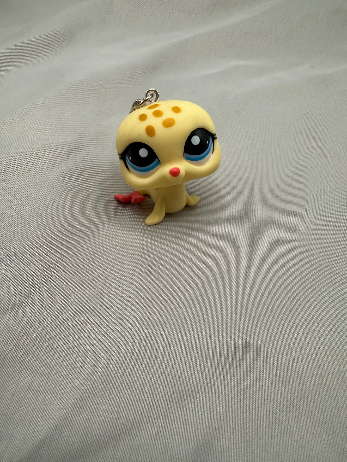 Small yellow creature figurine with black eyes and red nose on a gray fabric background