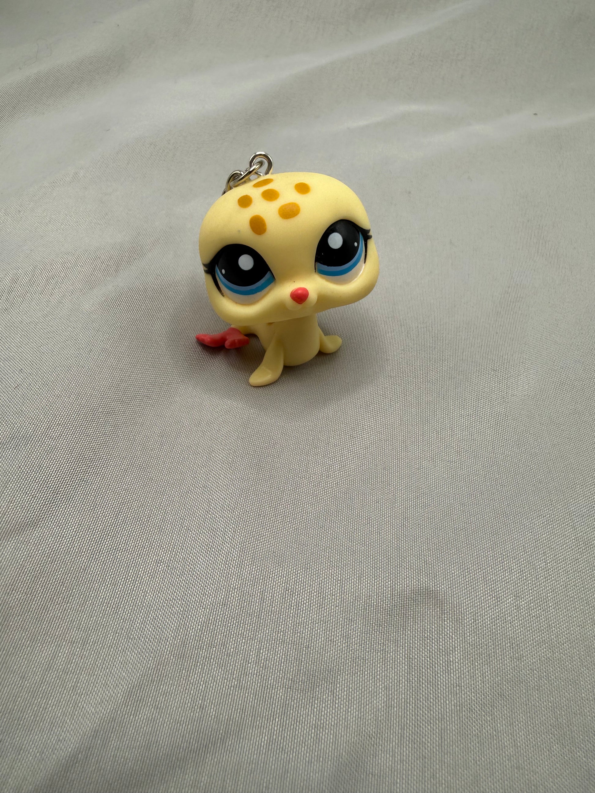Small yellow creature figurine with black eyes and red nose on a gray fabric background