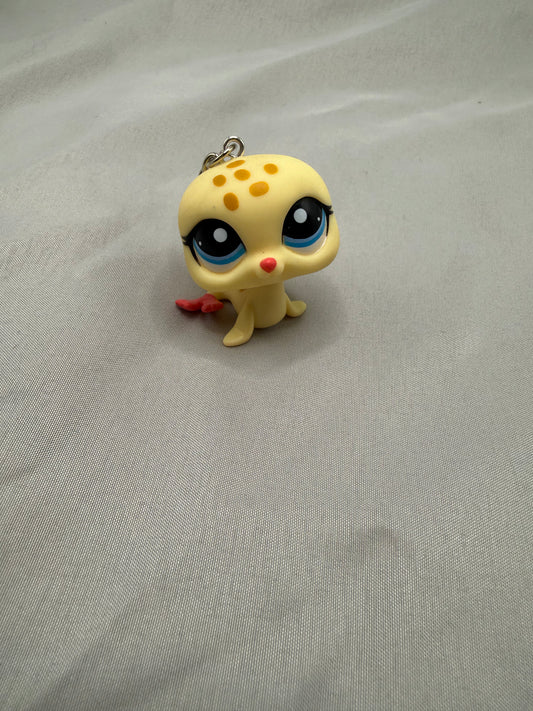 Small yellow creature figurine with black eyes and red nose on a gray fabric background