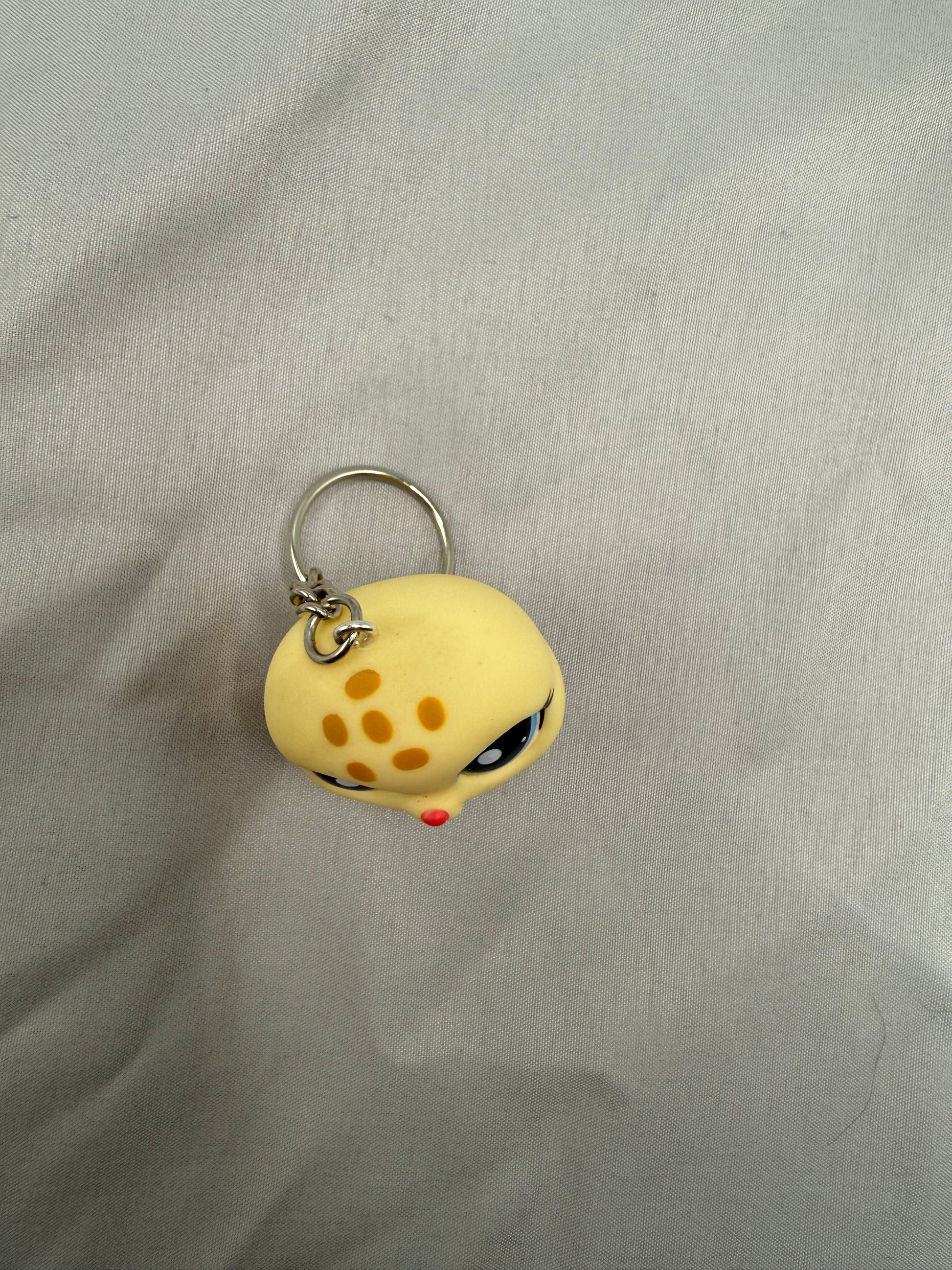 Yellow cartoon-like keychain with a small face on a gray fabric background