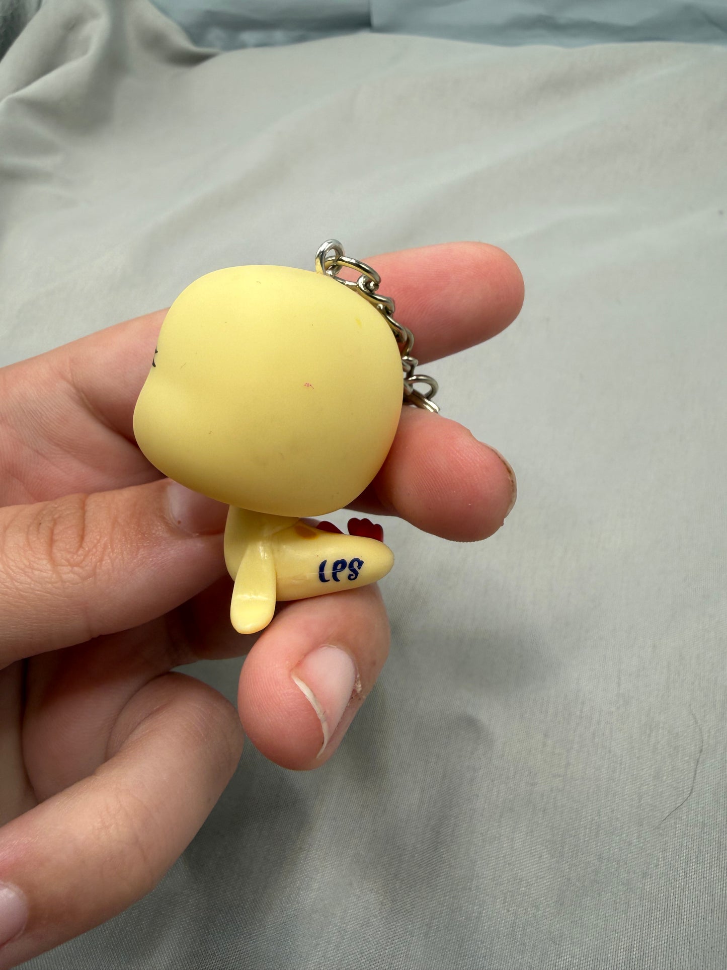 Yellow keychain figure with 'lps ' text held in a hand against a gray background