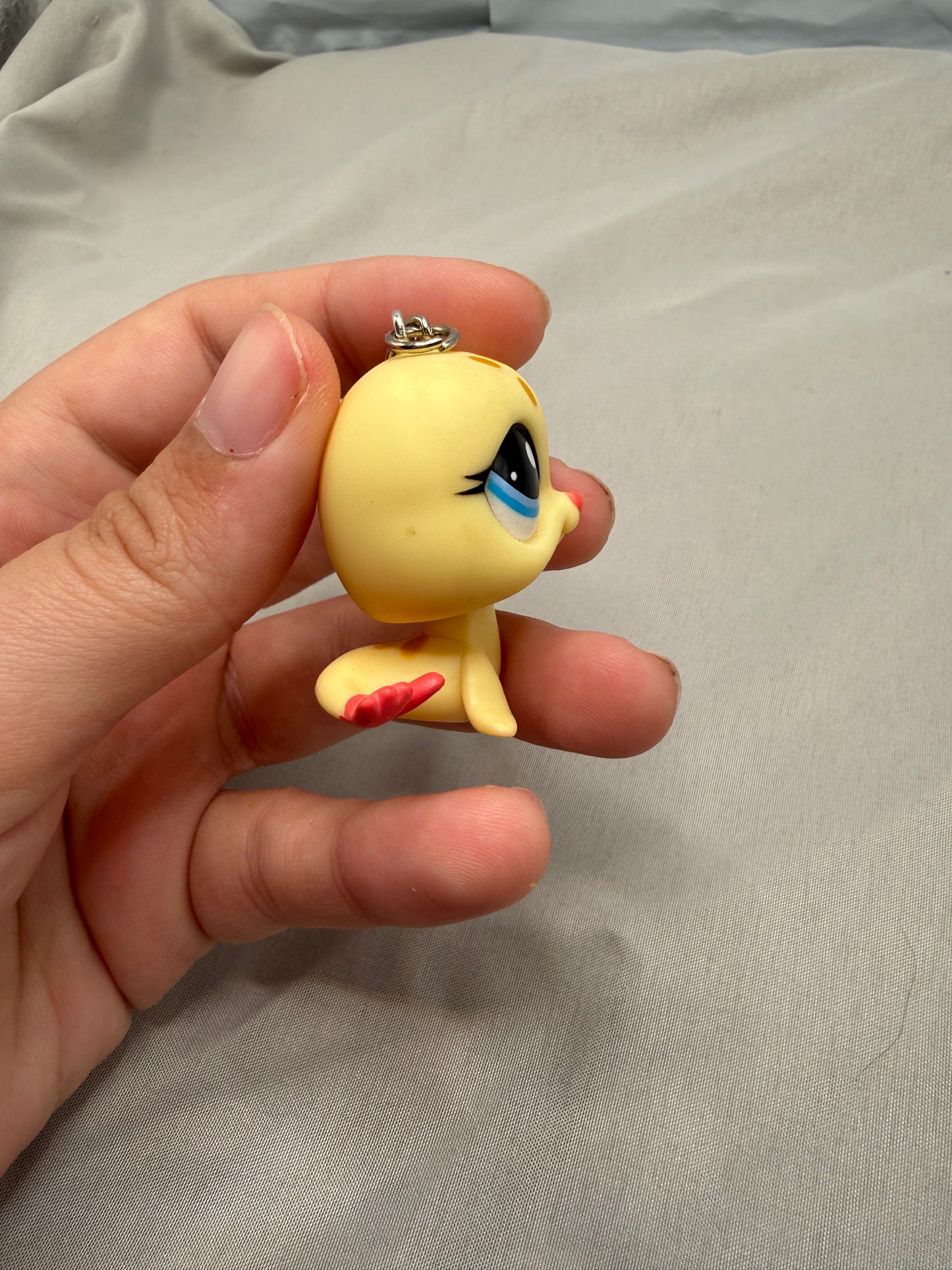 Hand holding a small yellow figurine with blue eyes and red fin on a gray fabric background