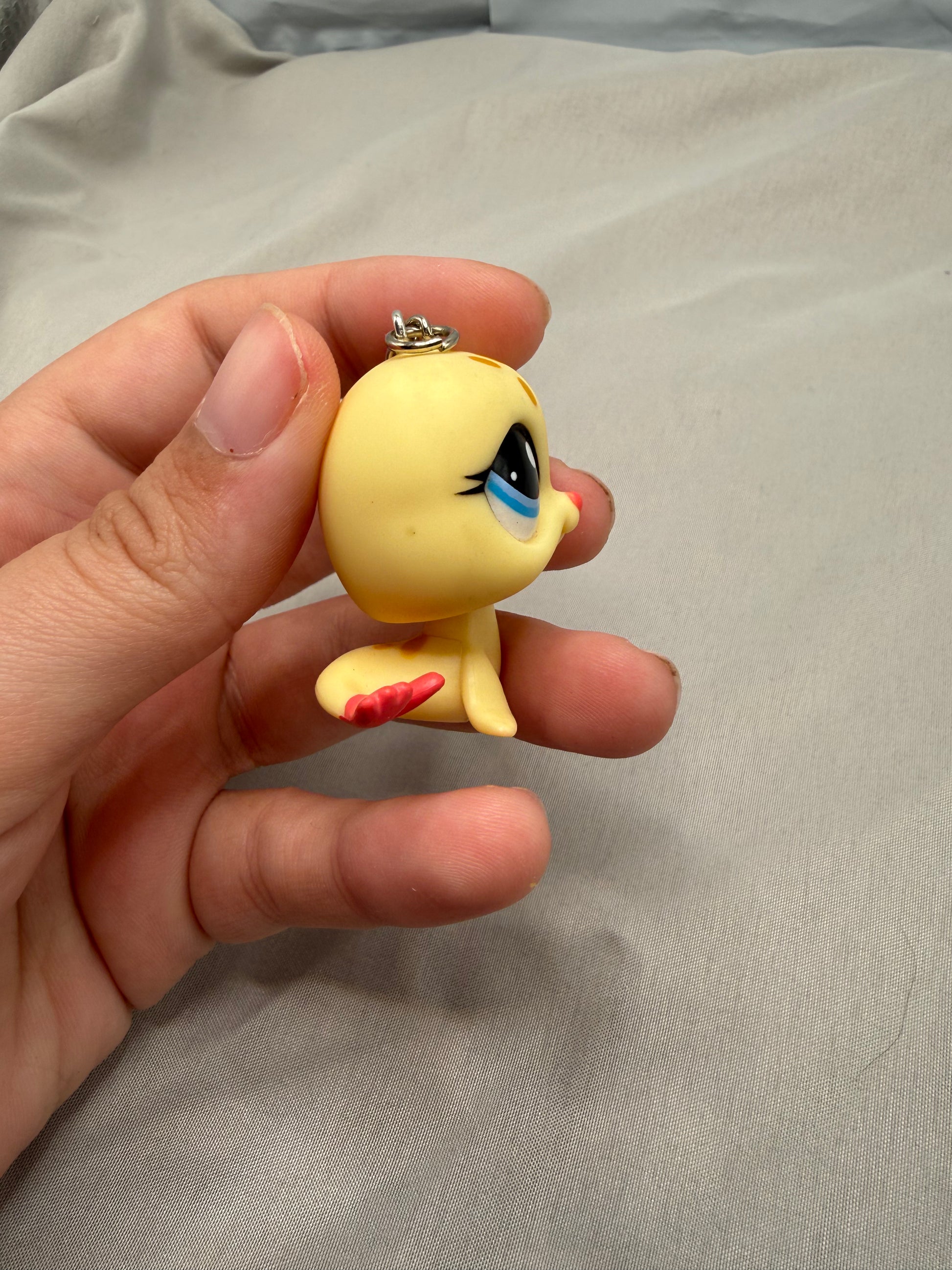 Hand holding a small yellow figurine with blue eyes and red fin on a gray fabric background