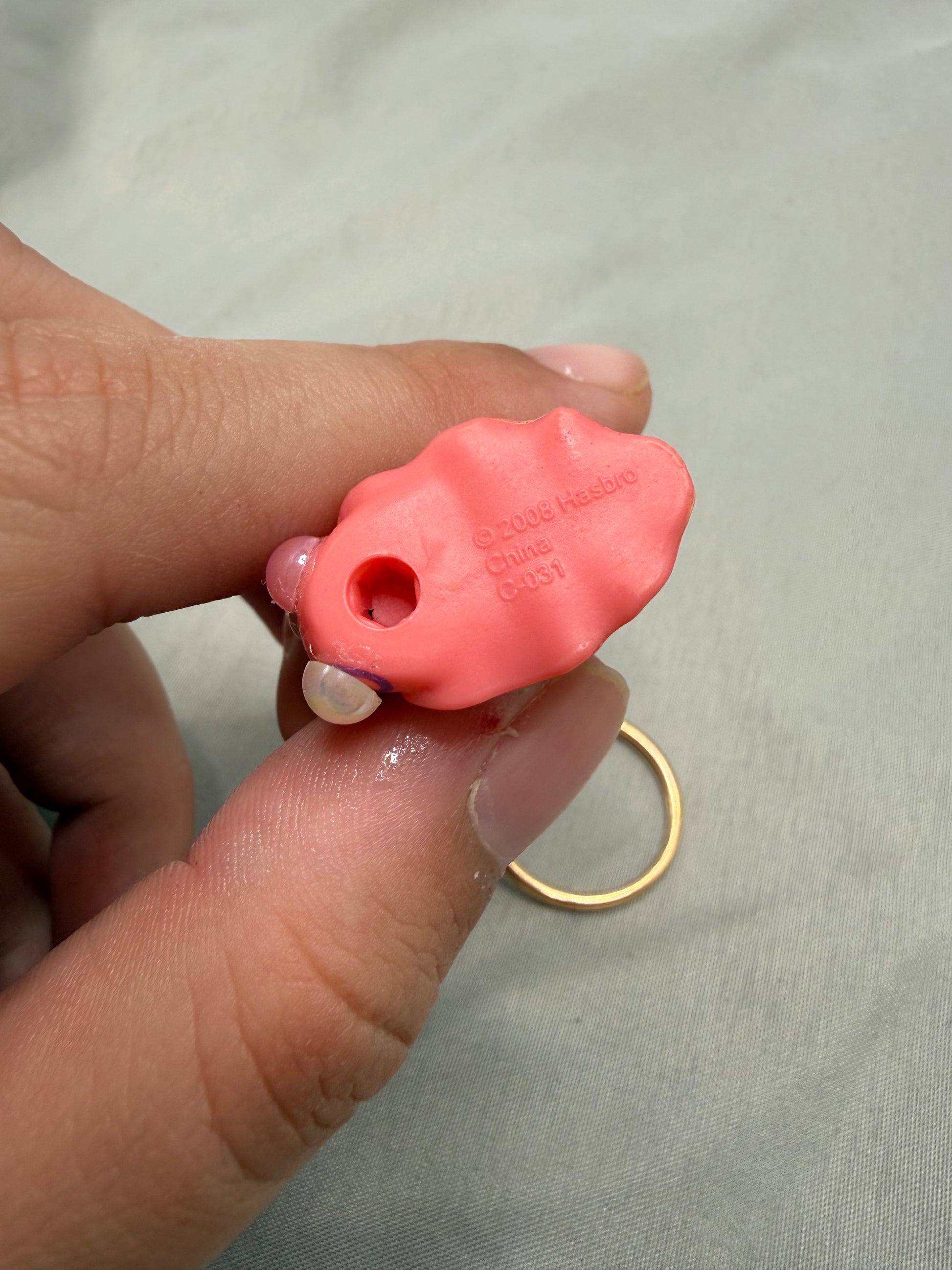 Hand holding a small pink snail toy with a brand name on a light gray background