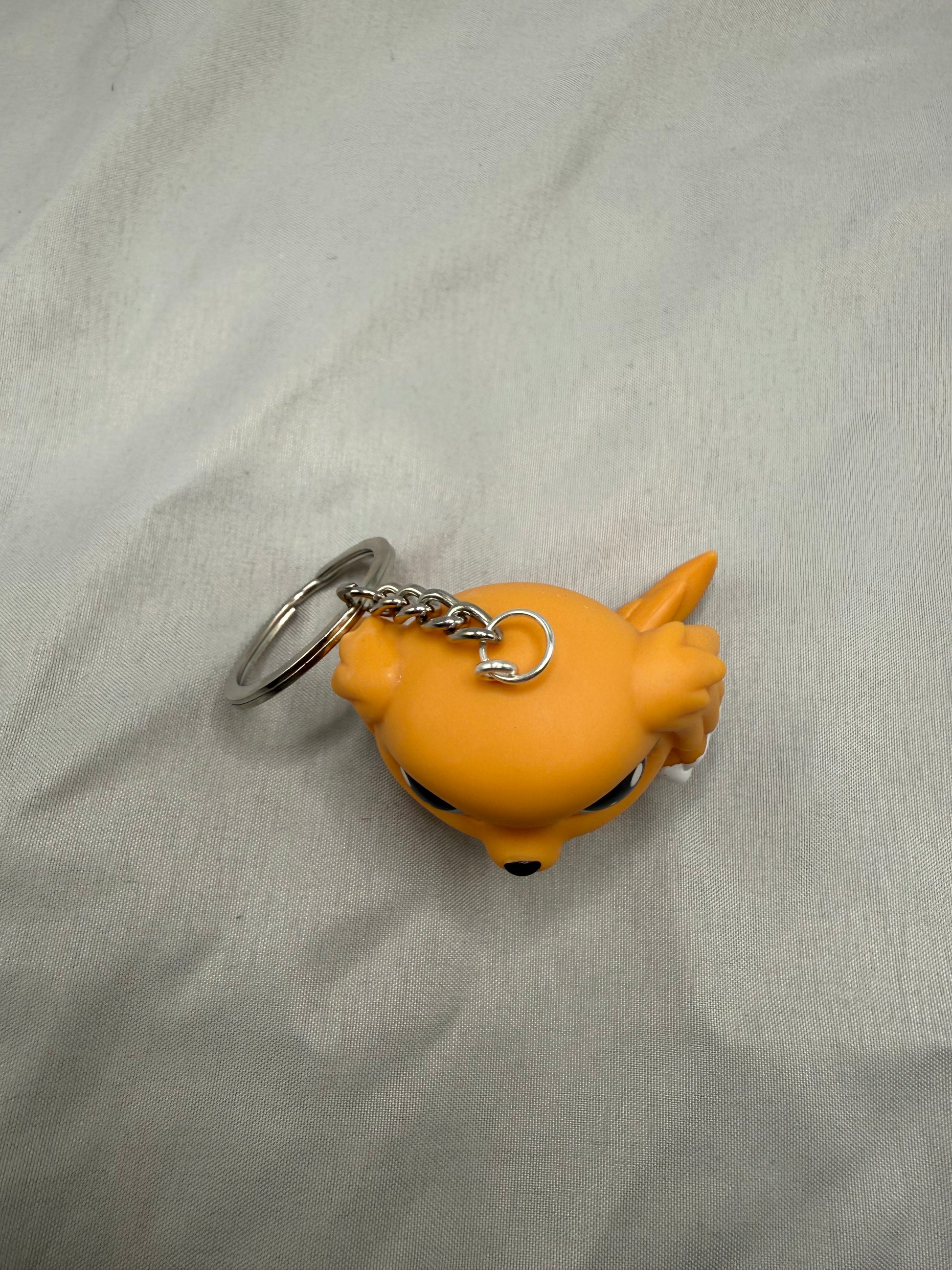 Orange cartoon-like keychain on a light gray fabric background
