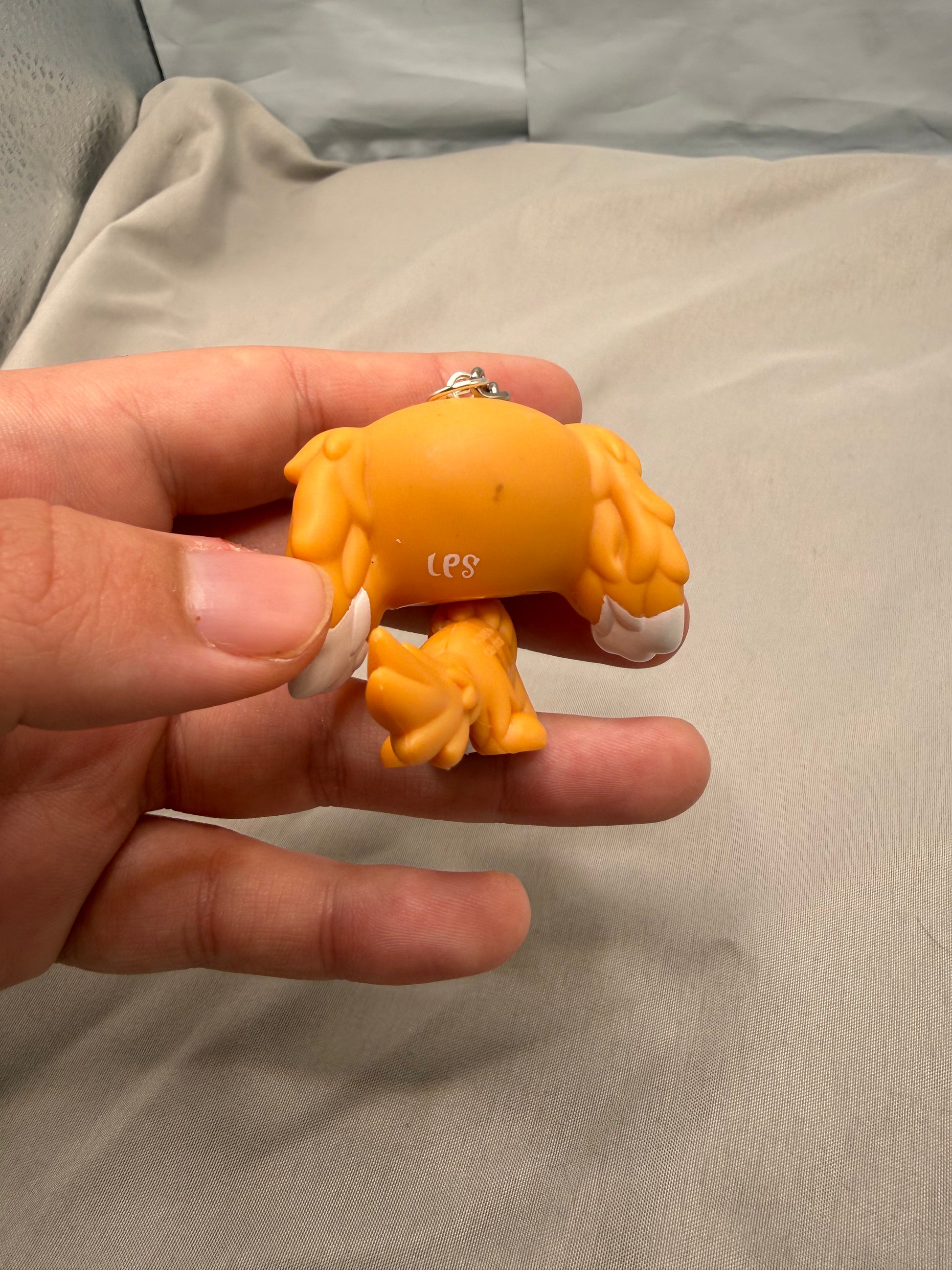 Hand holding a small orange figurine with white accents on a beige surface