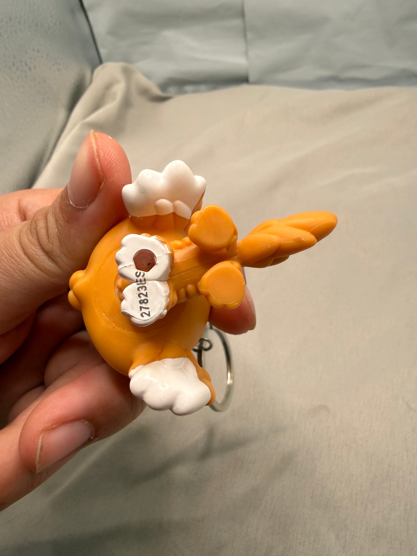 Hand holding a small orange and white figurine against a neutral background