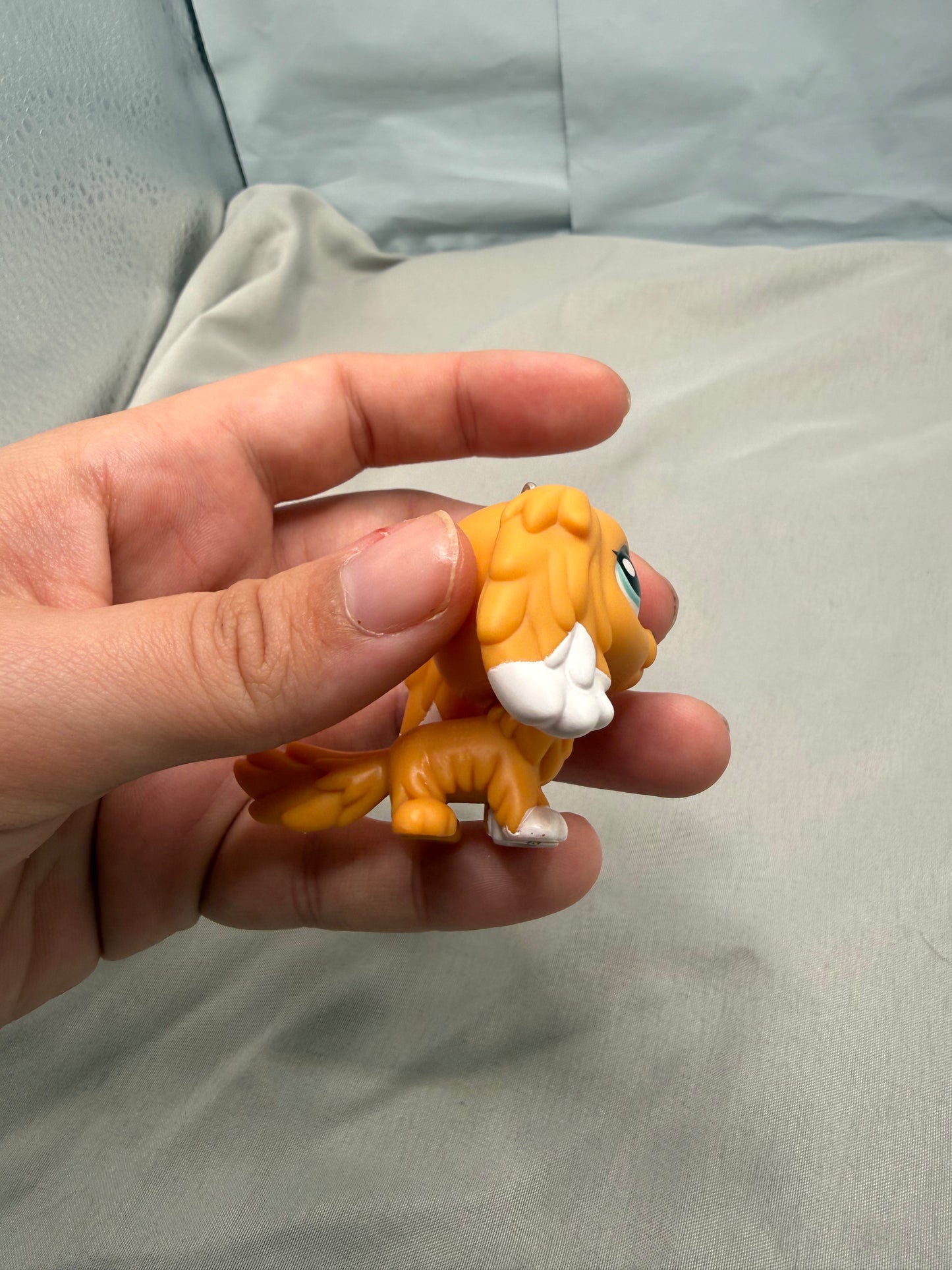Hand holding a small orange toy figure against a light gray background