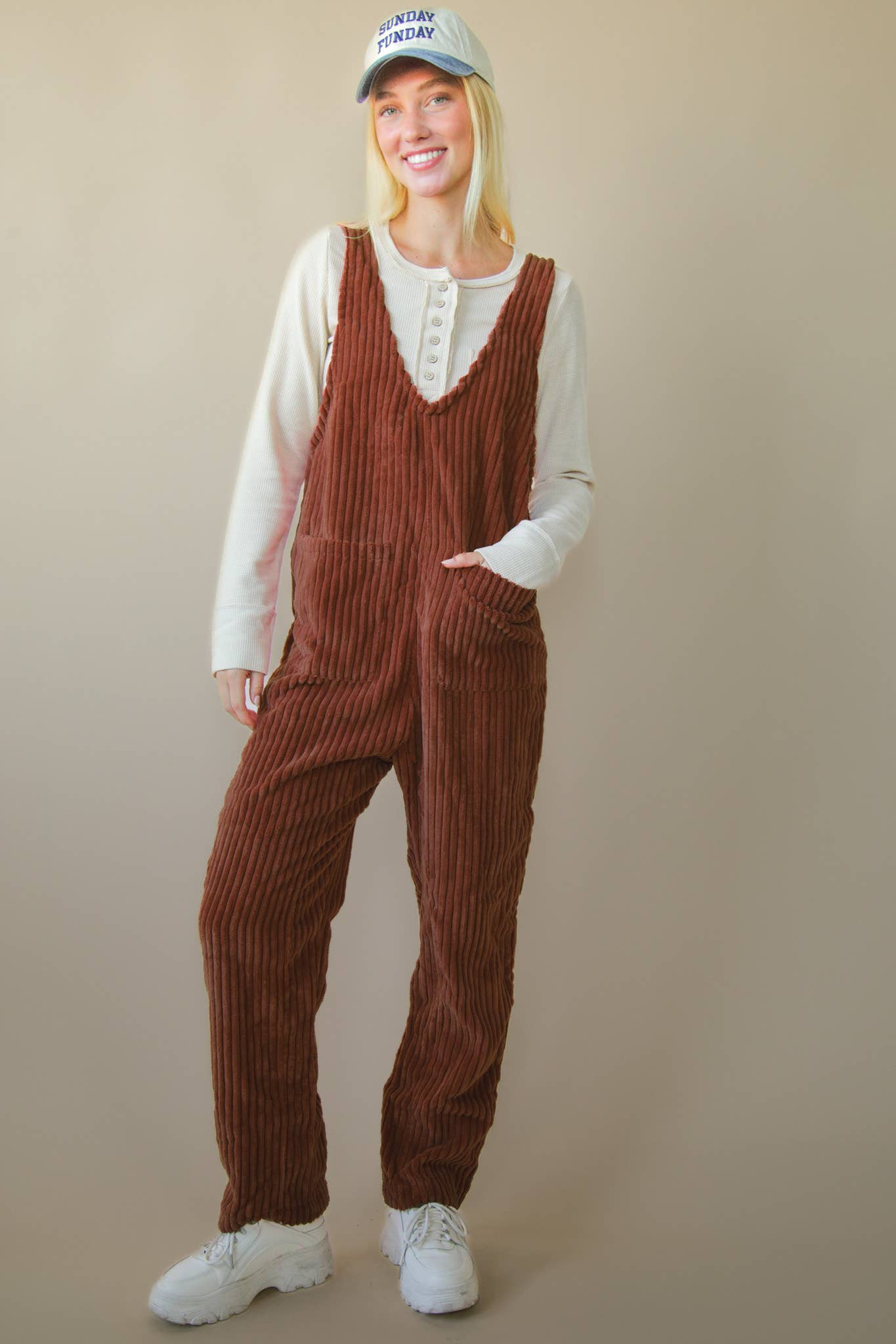 Person wearing brown corduroy overalls with a plain background