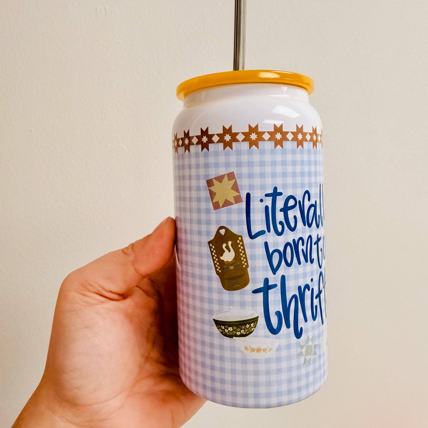 Hand holding a can with decorative design and text on a plain background