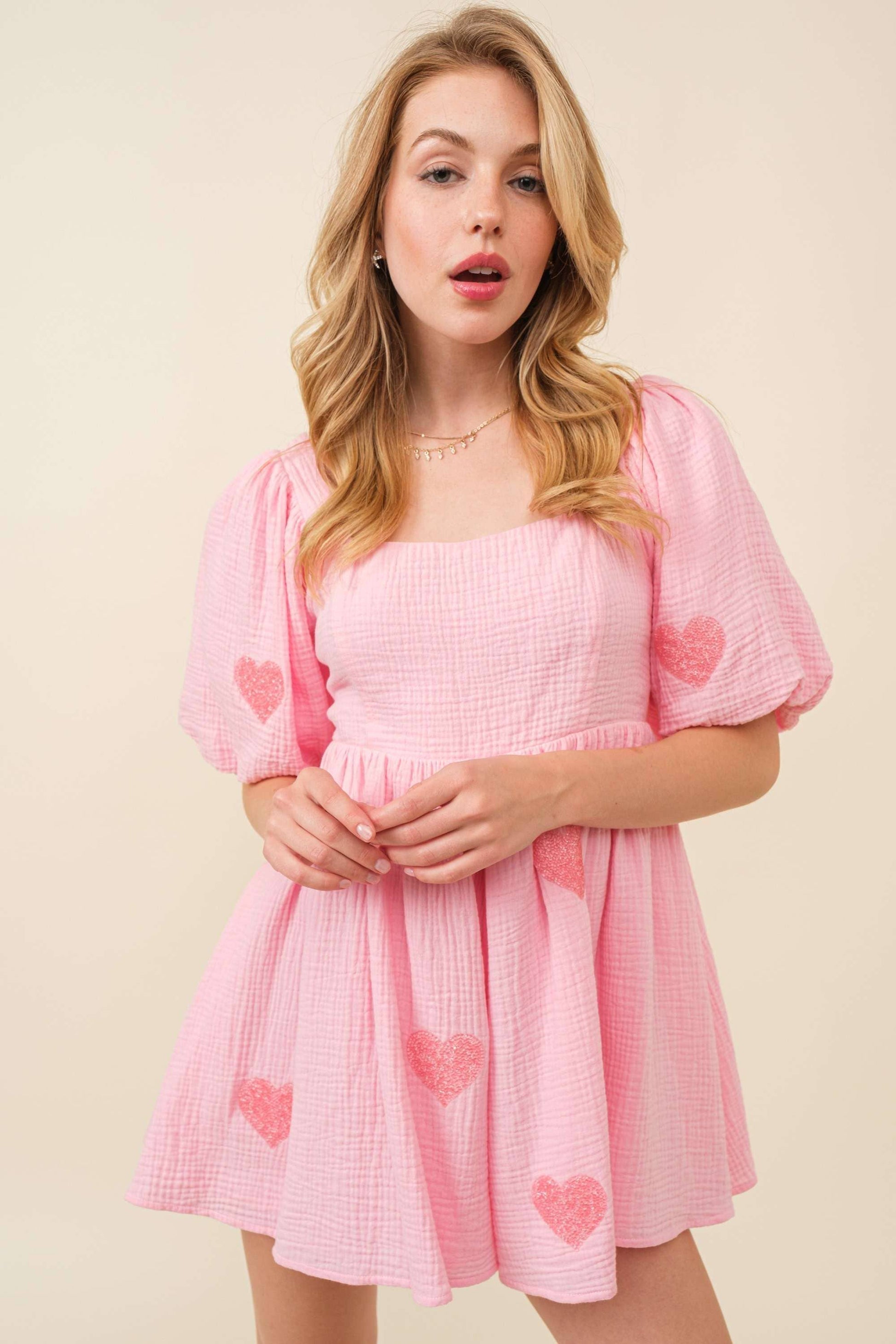 Woman wearing a pink dress with heart patterns on a beige background