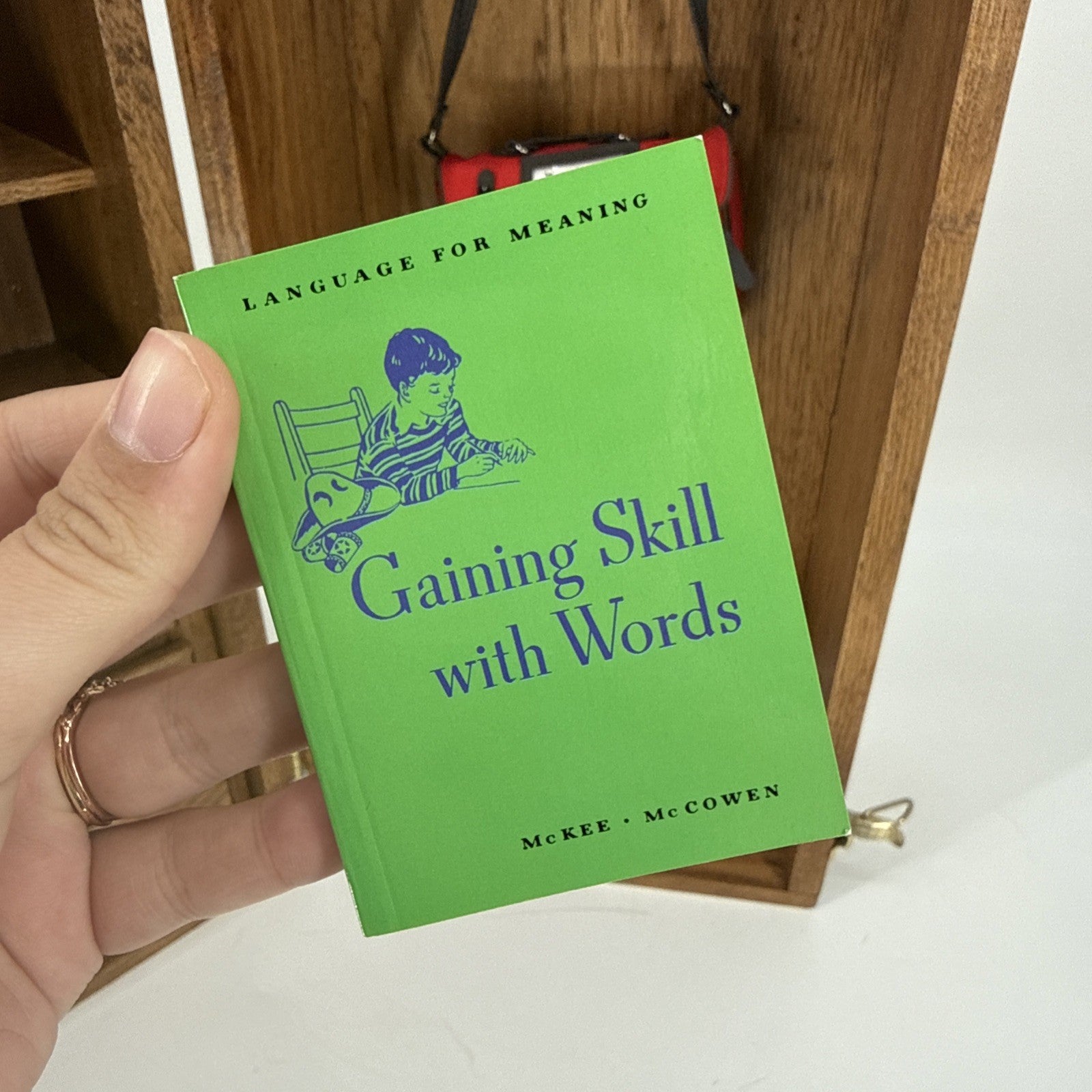 Hand holding a green book titled 'Gaining Skill with Words' against a wooden background.