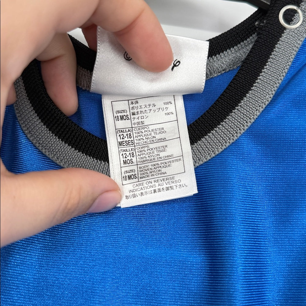 Close-up of interior care and size tag on blue Walt Disney World Mickey Mouse basketball baby romper, showing fabric details and shoulder snap