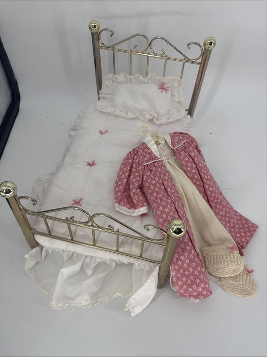 Miniature brass bed with white bedding and pink floral clothes on a white background