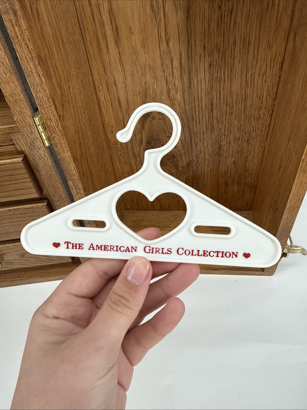 White hanger with heart design held by a hand in front of wooden furniture.