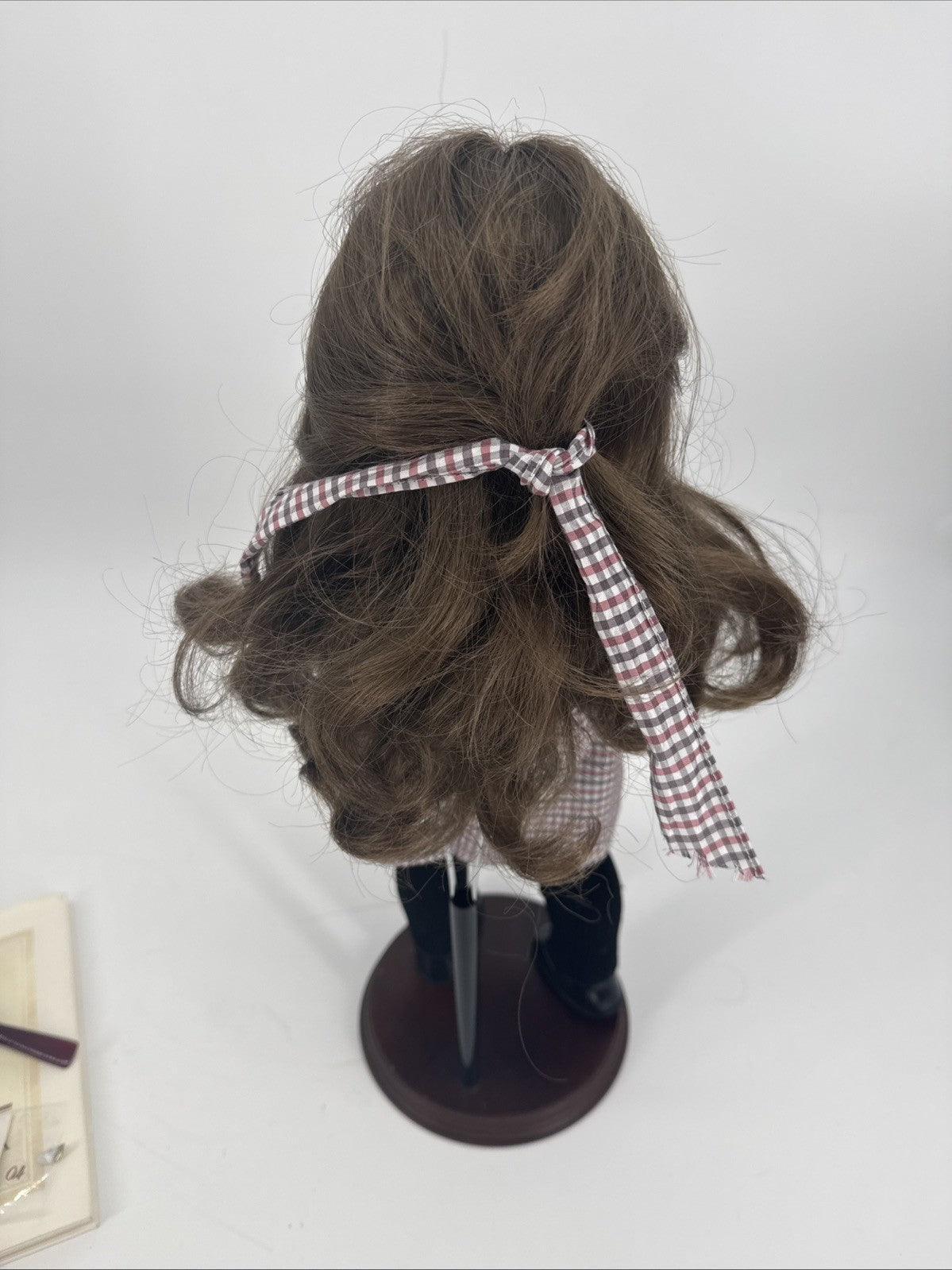 Brown wig on a mannequin head with a red and white checkered ribbon against a white background